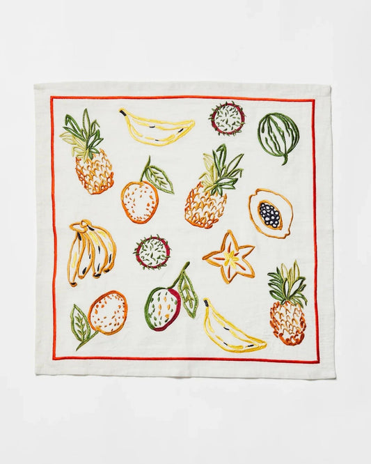 The TROPICS MULTI EMBROIDERED NAPKIN by Bonnie and Neil features a striking design with vibrant summer colors that include tropical fruits such as pineapples, bananas, watermelon, and star fruits, all beautifully framed by a bold red border.