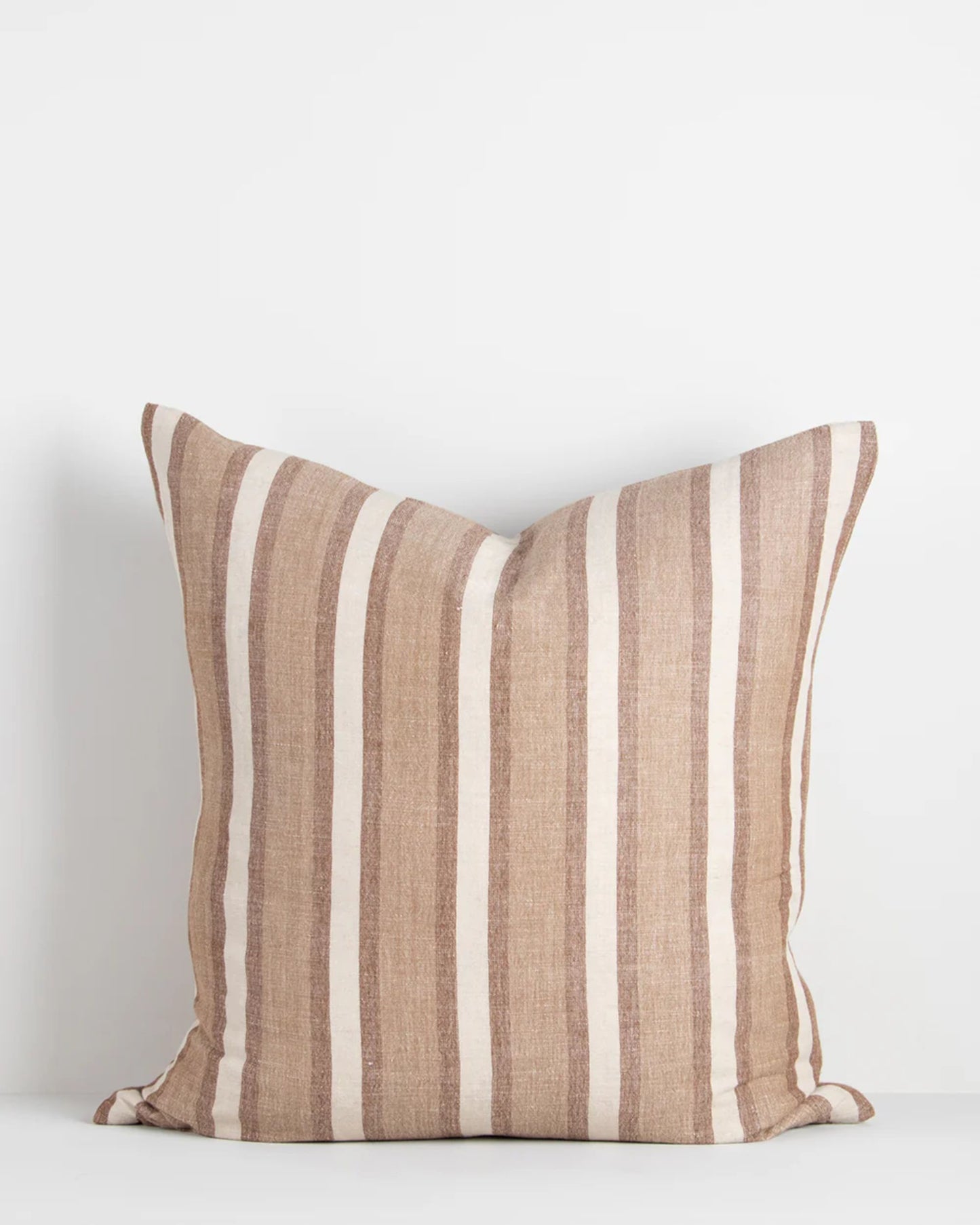 The BRIGHTON CUSHION by Baya is a square pillow featuring vertical beige and white stripes on a plain white background. Crafted from natural fibers, it offers a soft and plush feel with slightly creased fabric along the edges.