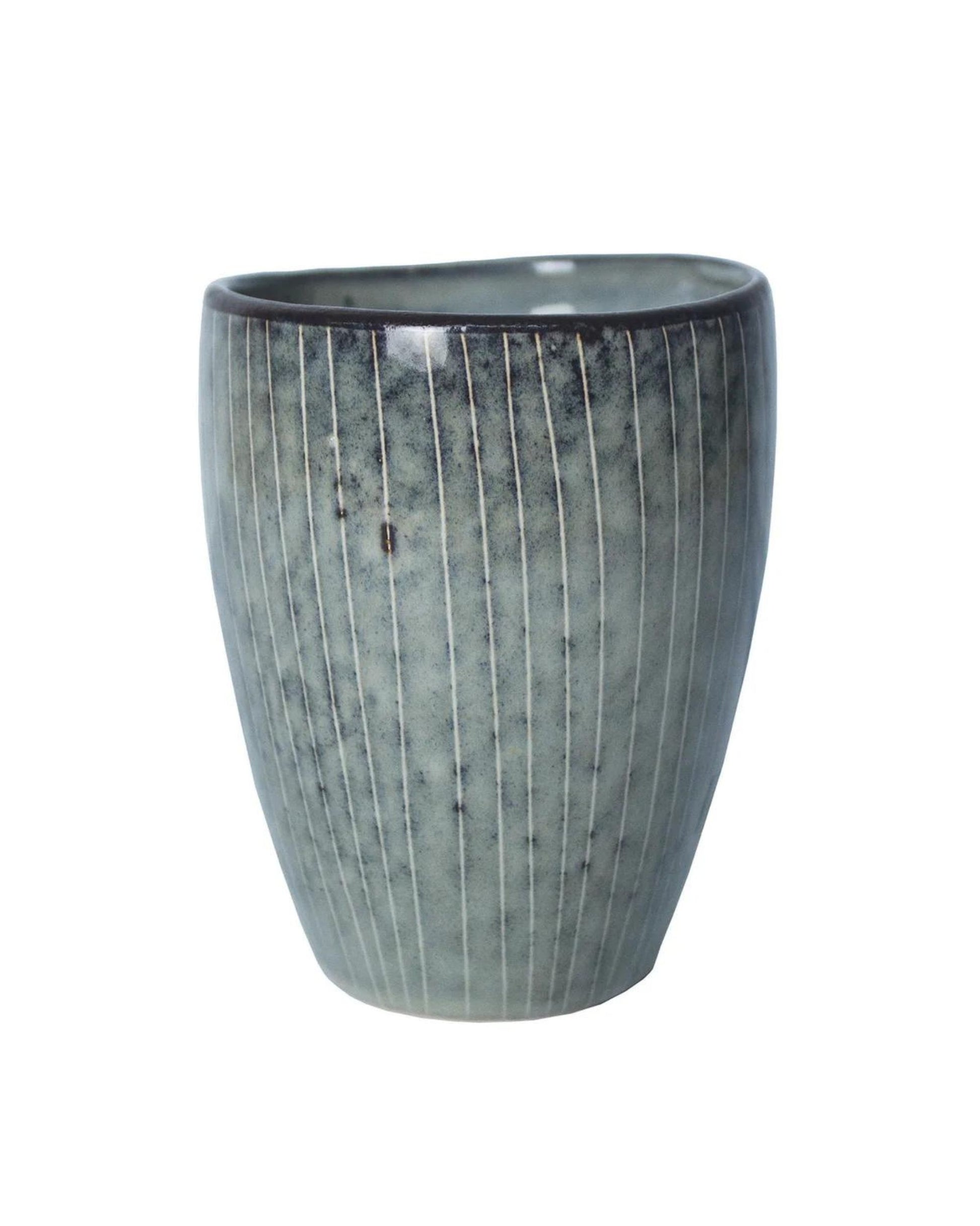 The MUG - NO HANDLE by Broste is a textured ceramic piece without a handle, showcasing a subtle greenish-blue hue complemented by vertical line patterns. Its rounded shape and slightly irregular top rim enhance its rustic, handmade look, encapsulating minimalist design.