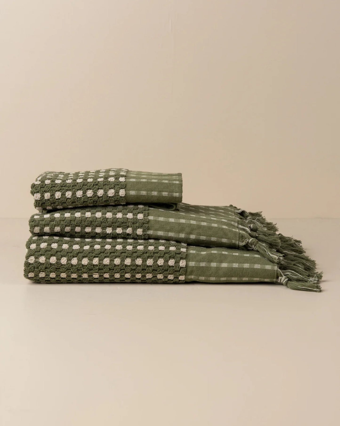 Three CHICKPEA BATH SHEETS in a checkered pattern and fringed edges, crafted from soft and detailed Turkish cotton by Saarde, are stacked on a neutral surface. These super absorbent green towels add a touch of elegance to home decor or bathroom settings.