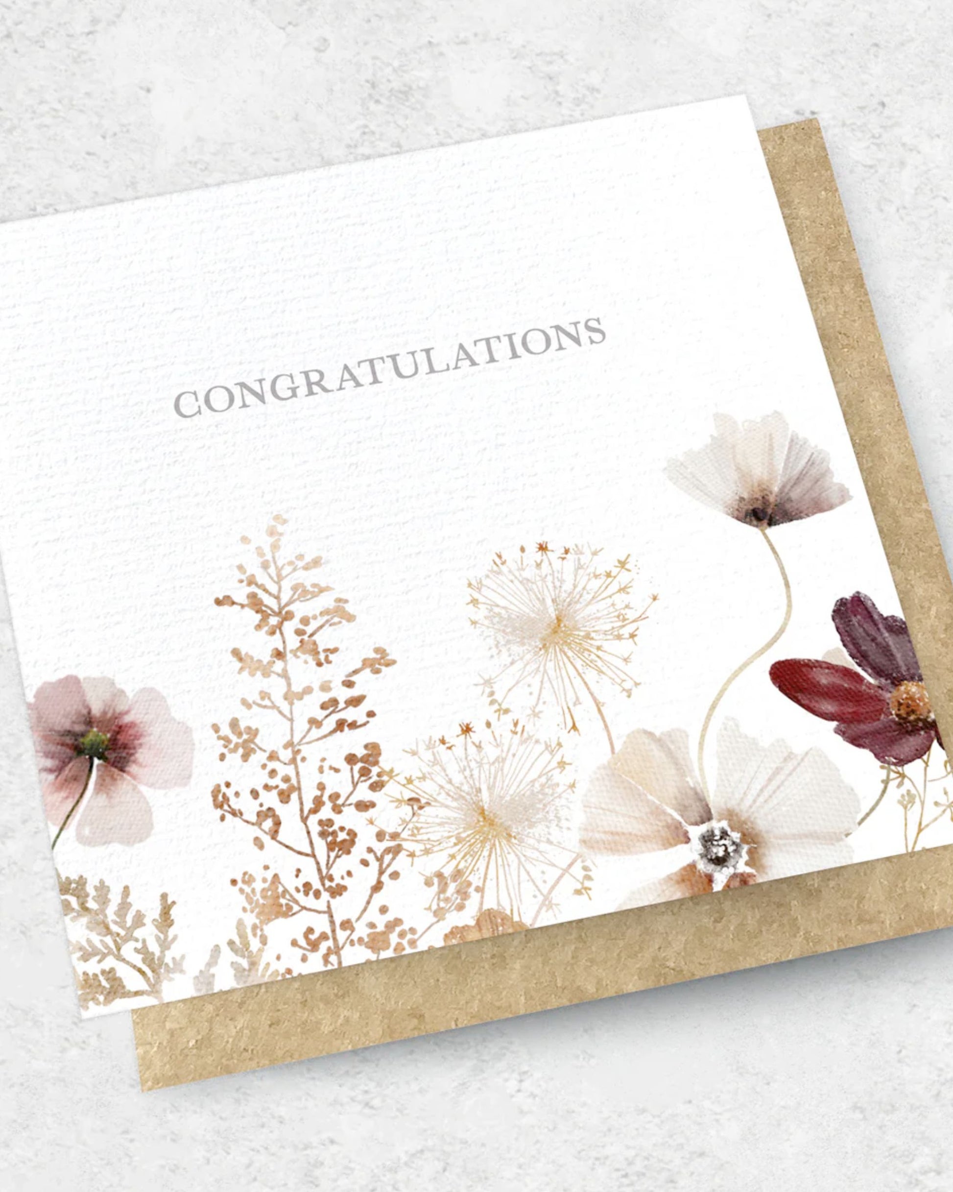 The "CONGRATULATIONS FLOWERS - GREETING CARD" by Ink Bomb showcases elegant floral illustrations with watercolor-style flowers and foliage in gentle neutral shades. This premium card features a textured surface and comes with a kraft envelope.