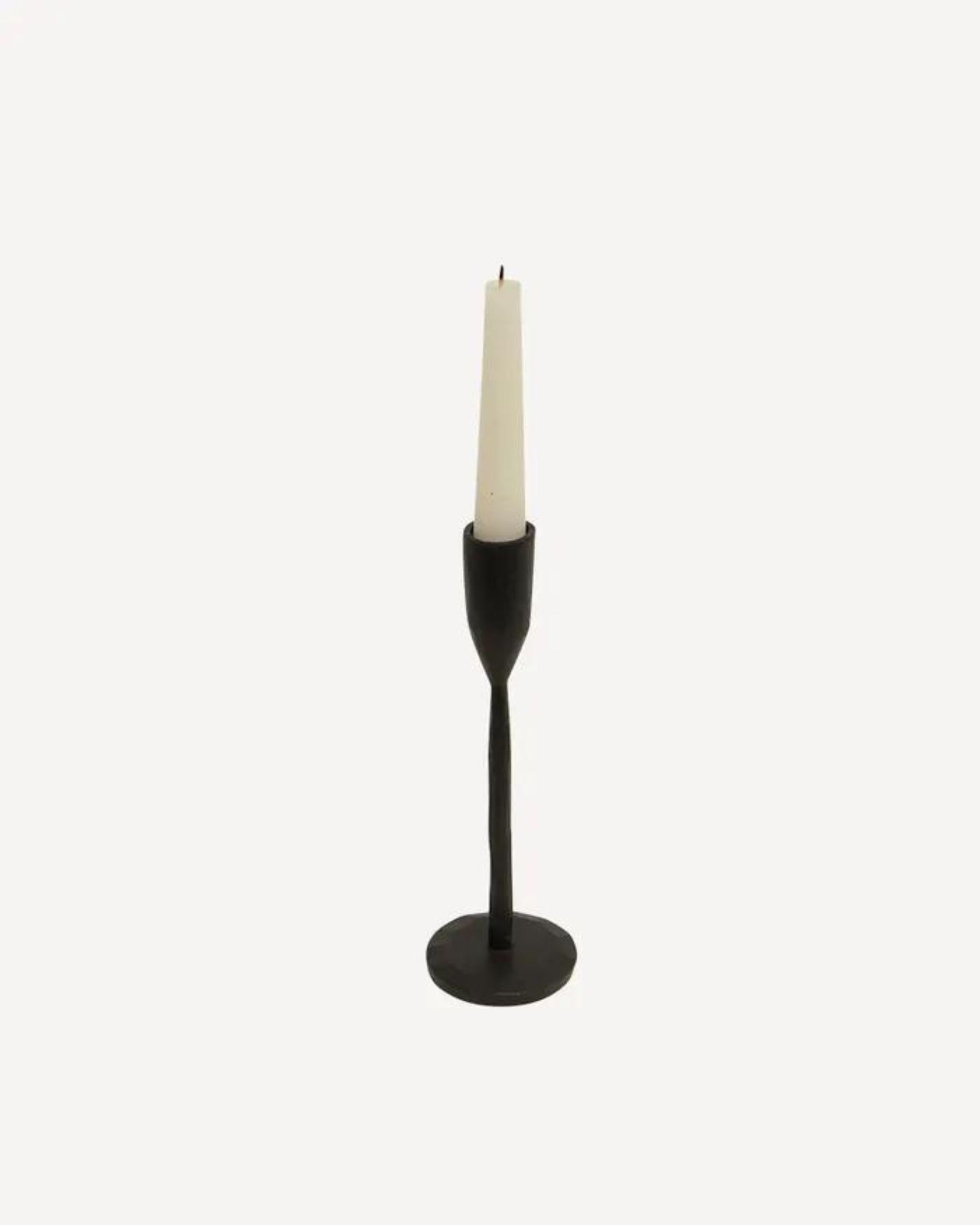 A white taper candle sits elegantly in the DAX CANDLEHOLDER- BLACK by French Country, a hand-forged matte black candlestick with a round base, set against a plain white background.