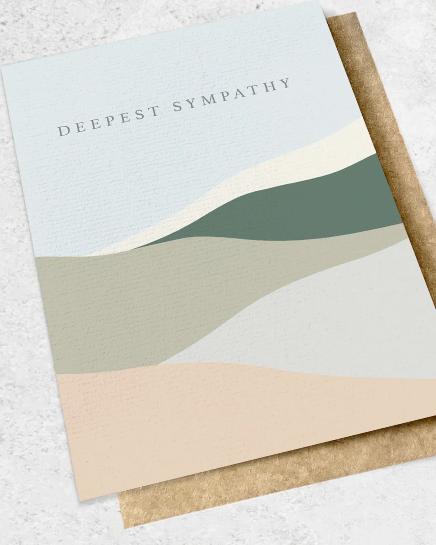 The DEEPEST SYMPATHY - GREETING CARD by Ink Bomb showcases a premium textured design with abstract wavy patterns in muted green, beige, and cream tones. The heartfelt message "Deepest Sympathy" adorns the top of the card. Accompanied by a matching kraft envelope, this elegant card serves as a meaningful expression of condolences.