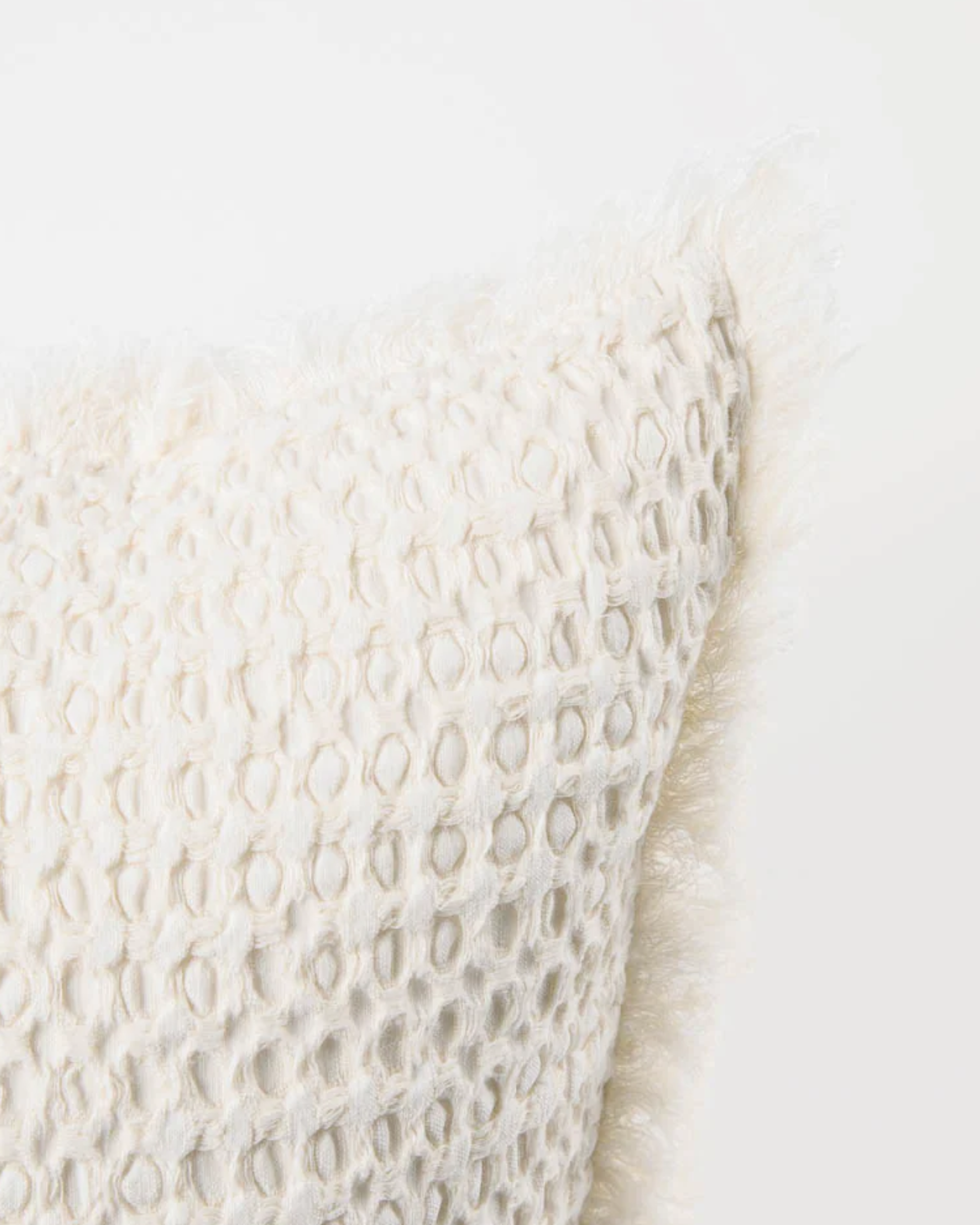 A close-up of the ELEMENT CUSHION - IVORY 40x60 by Eadie, which is crafted from a linen and cotton blend. It features a textured honeycomb pattern and soft, fluffy edges that introduce a subtle boho feel against a plain background.