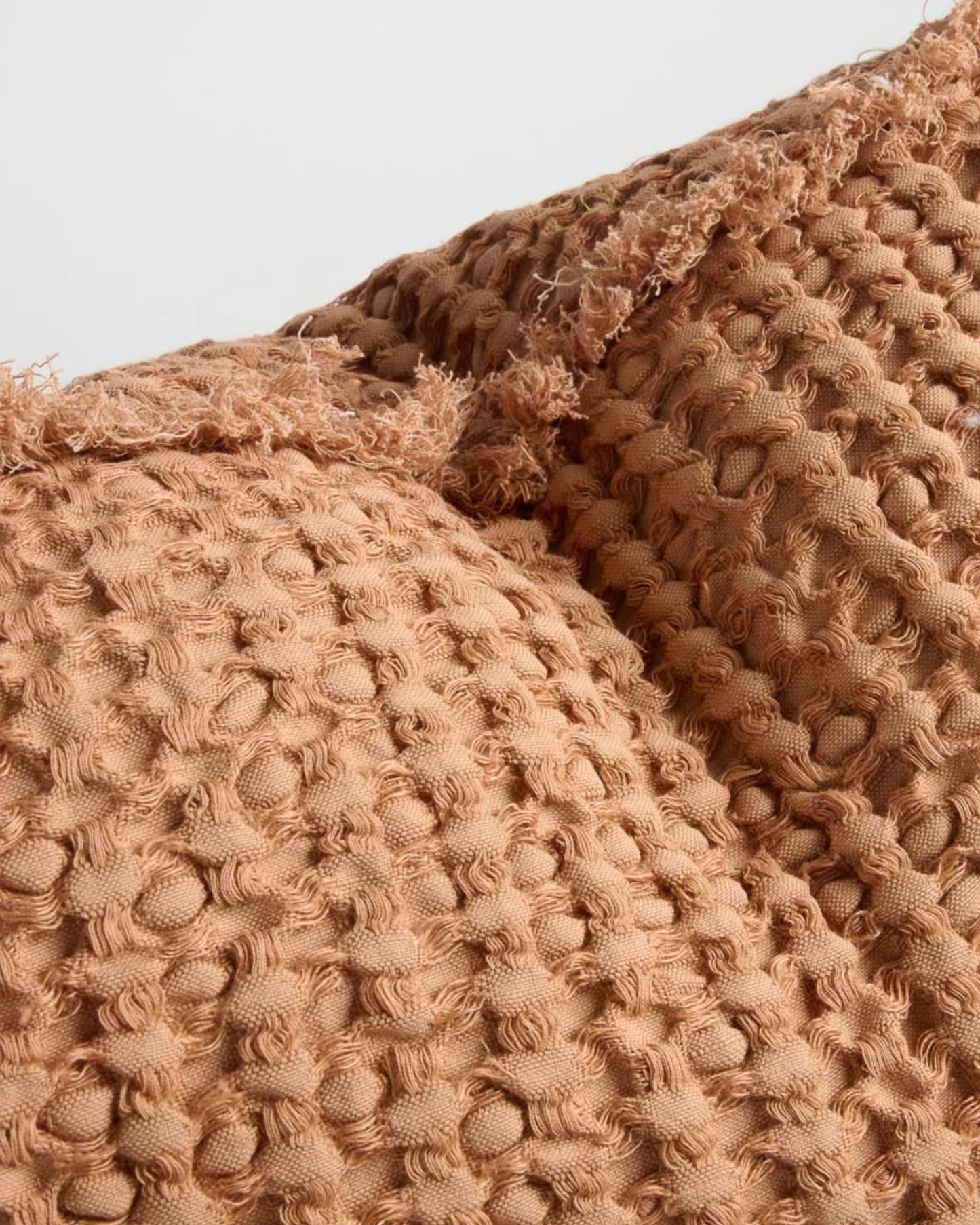 Close-up of the Element Cushion - Orchre 40x60 by Eadie, featuring a textured, woven loop pattern with frayed edges. The fabric's warm, earthy brown color with an ochre tone adds a boho effect.