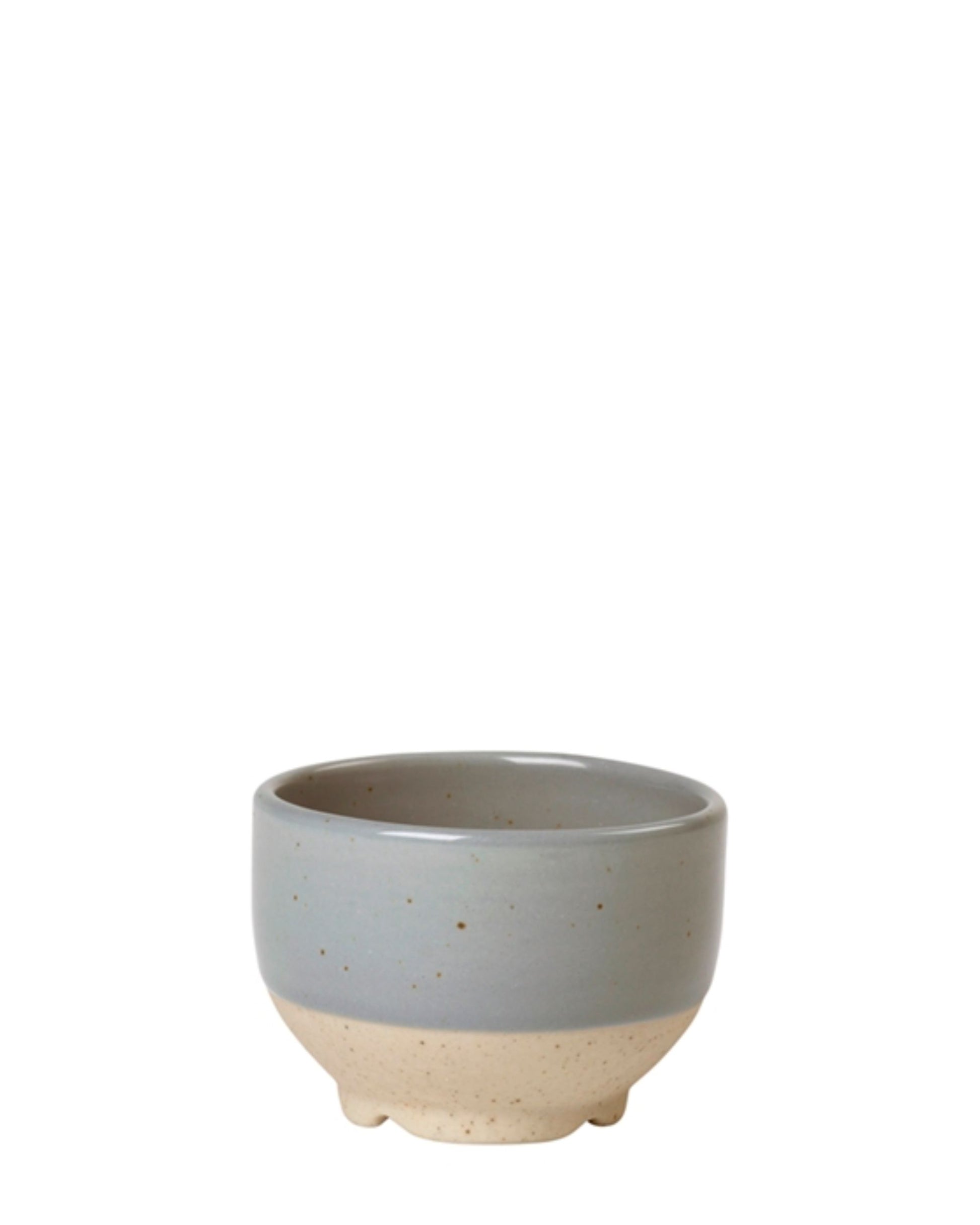 The ELI MINI BOWL by Broste is a small, round ceramic bowl showcasing a beautiful two-tone design with the top half in muted gray and the bottom in natural beige. It features a smooth, glossy finish with hints of reactive glaze, embodying the simple elegance of minimalist Japanese tableware.