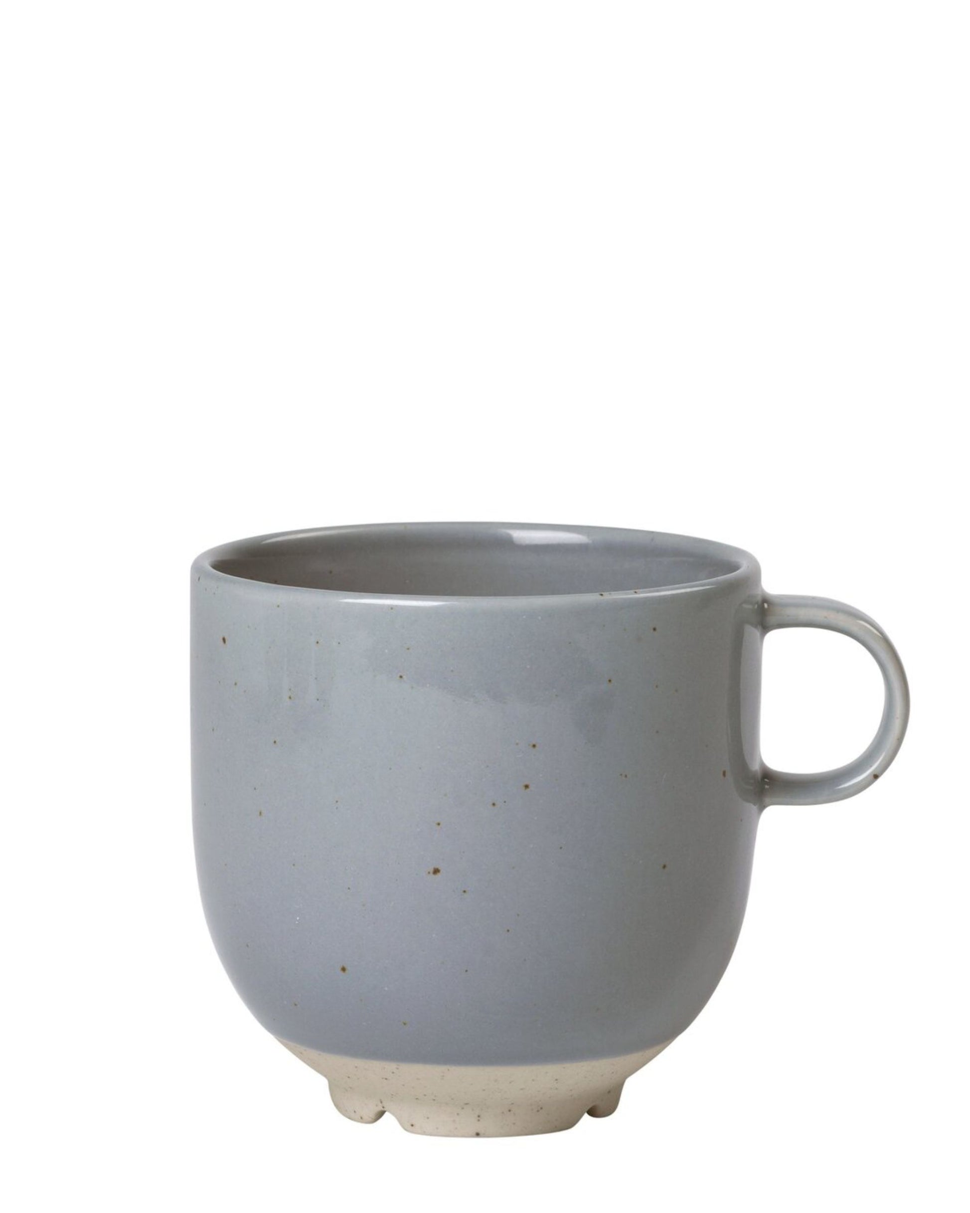 The ELI MUG W/HANDLE by Broste is a plain gray ceramic mug with a handle, featuring a reactive glaze that adds Japanese-inspired elegance to its speckled texture. It showcases an unglazed beige bottom edge and is part of the Eli collection, set against a white background.