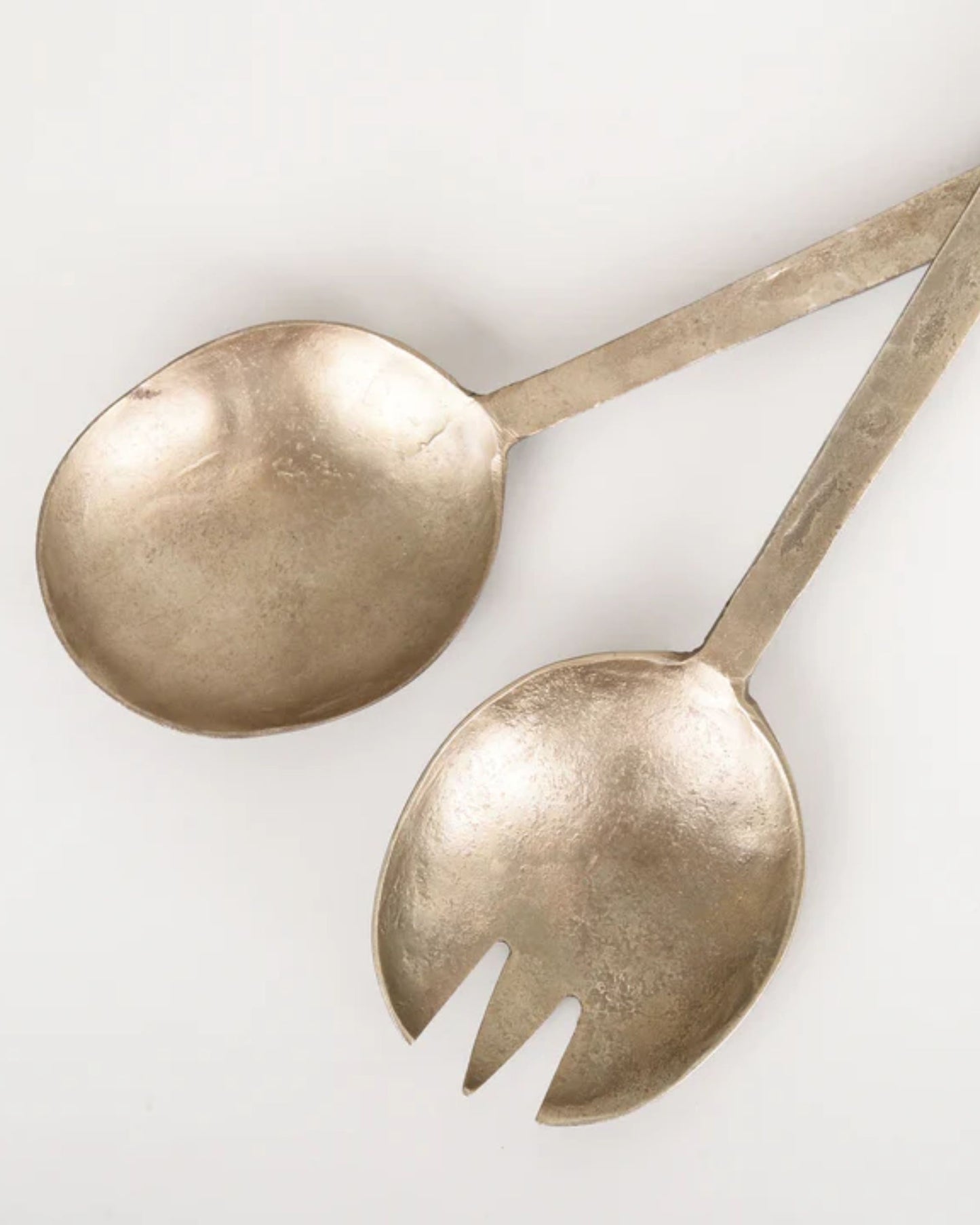 A pair of vintage silver serving utensils from New Direction is displayed against a plain white background. One is a spoon, and the other is a two-pronged fork. These Antique Flat Handle Serving Spoons feature a slightly tarnished, reflective surface that speaks to their rich history.