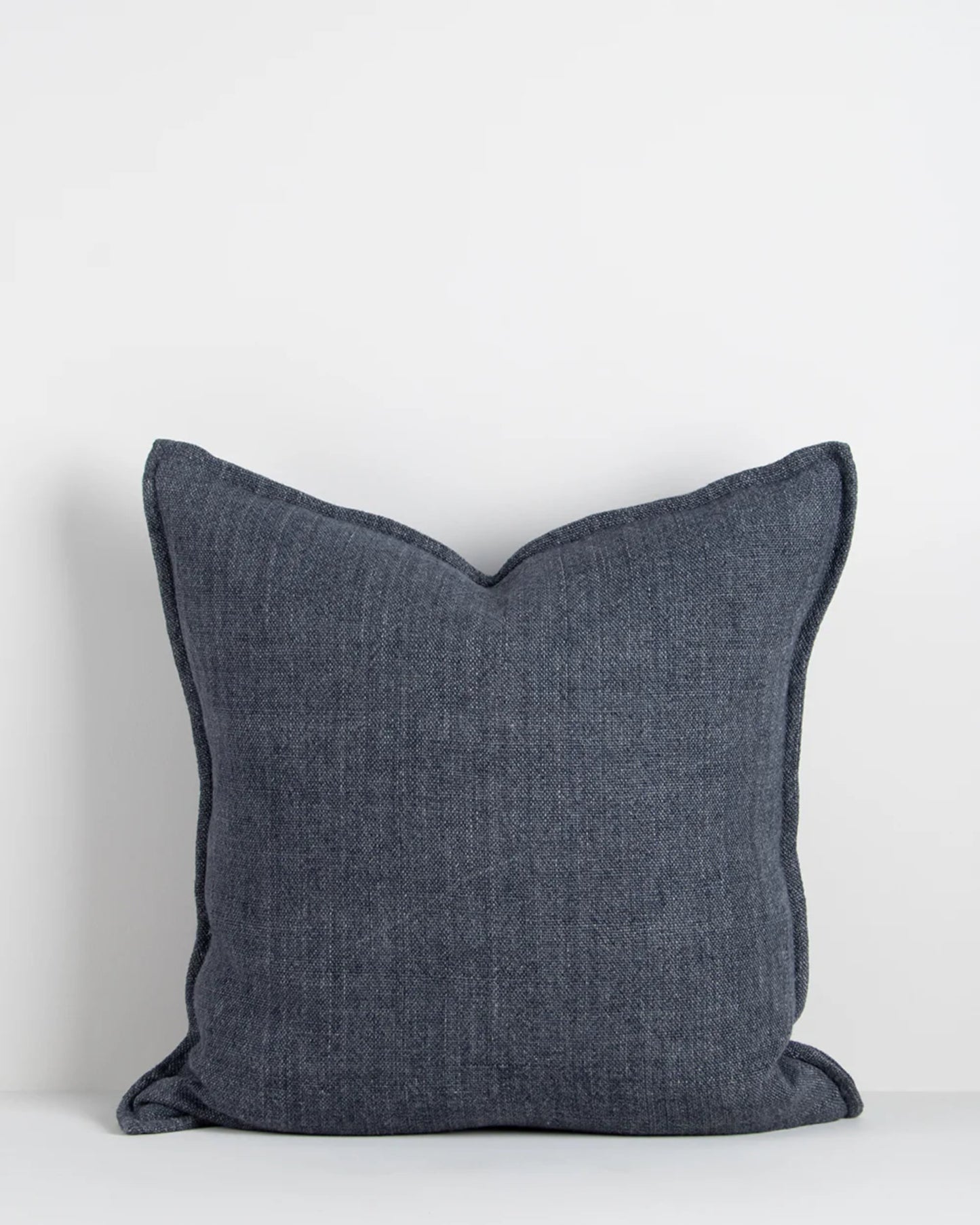 The FLAXMILL HANDWOVEN LINEN CUSHION by Baya, featuring a square shape and heavyweight weave in dark denim blue, sits against a plain light gray background, highlighting its minimalist and textured design.