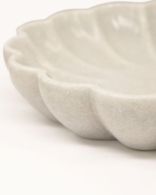 Close-up of the FLORA PLEATED MARBLE DISH - LARGE by Hawthorne, featuring a textured, scalloped-edge design in light gray ceramic on a white surface. Its organic shape and matte finish evoke the simple elegance typically associated with hand-carved marble items, enhancing its understated charm.