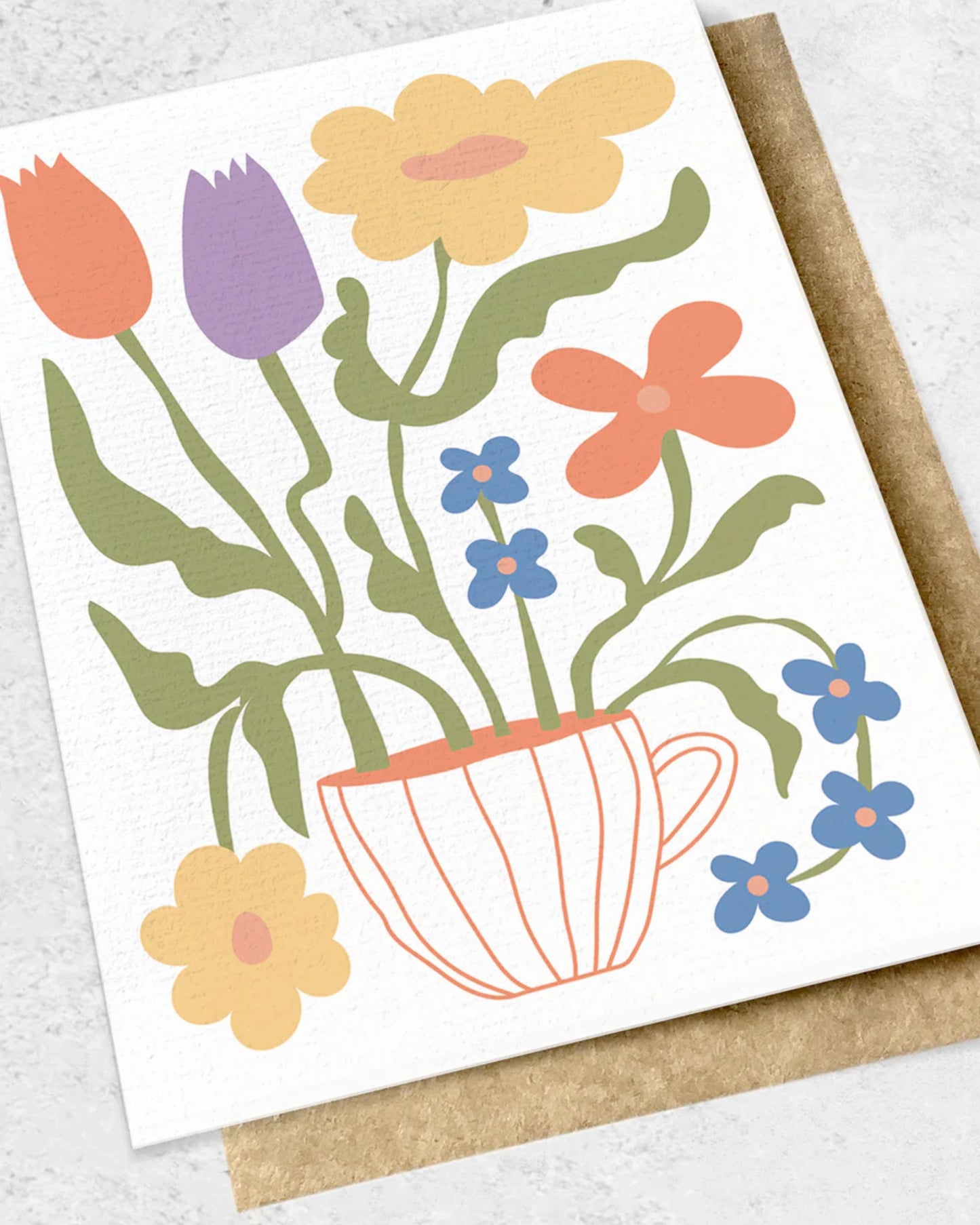 The FLORAL SUMMER ABSTRACT - GREETING CARD by Ink Bomb features a premium textured design with colorful flowers, including tulips and daisies, arranged in a teacup vase. The illustration is adorned with pastel shades of red, yellow, blue, and purple on a textured paper background and comes with a matching kraft envelope.