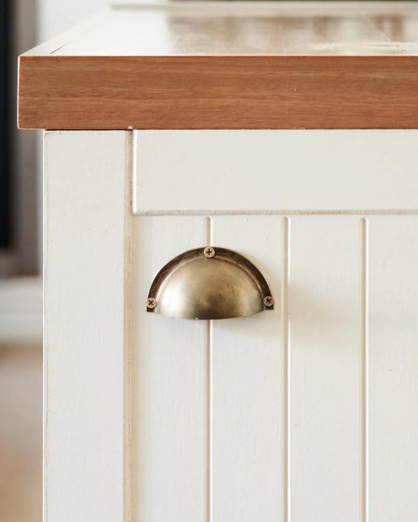 Close-up of a white cabinet with vertical paneling and a wooden countertop, reminiscent of a ship's galley kitchen. The cabinet is designed in Australia and features the elegant GALLEY DRAWER PULL by Society Ink, adorned with a brass cup handle.