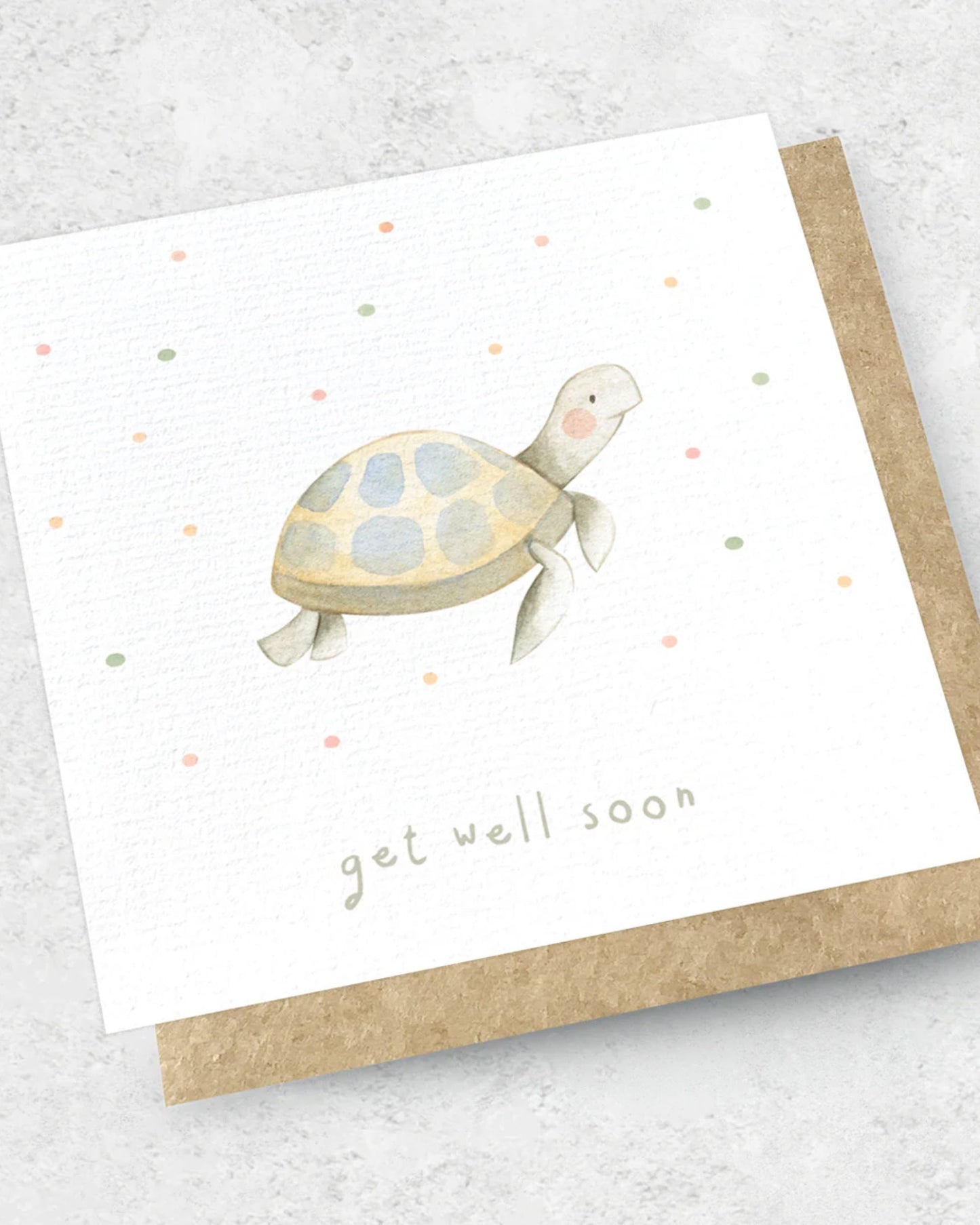 The "GET WELL SOON - GREETING CARD" by Ink Bomb features a watercolor turtle adorned with a shell of blue and brown spots, complemented by pastel dots in the background. The front displays the message "Get well soon," and it comes with a kraft envelope that enhances its natural appeal.