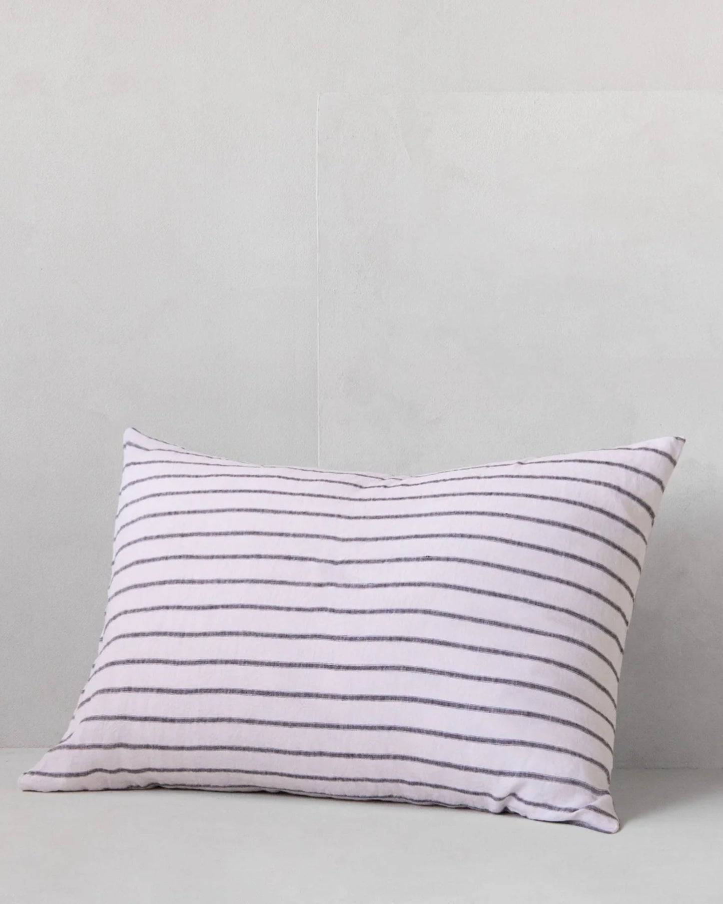 The HALE BASIX STRIPE PILLOWCASE, crafted by Hale Mercantile Co, features a white cover adorned with thin, evenly spaced black stripes. It is set against a light gray backdrop. Made from pure linen, this pillowcase provides a soft and cushioned feel that enhances the elegance of any linen bedding ensemble.