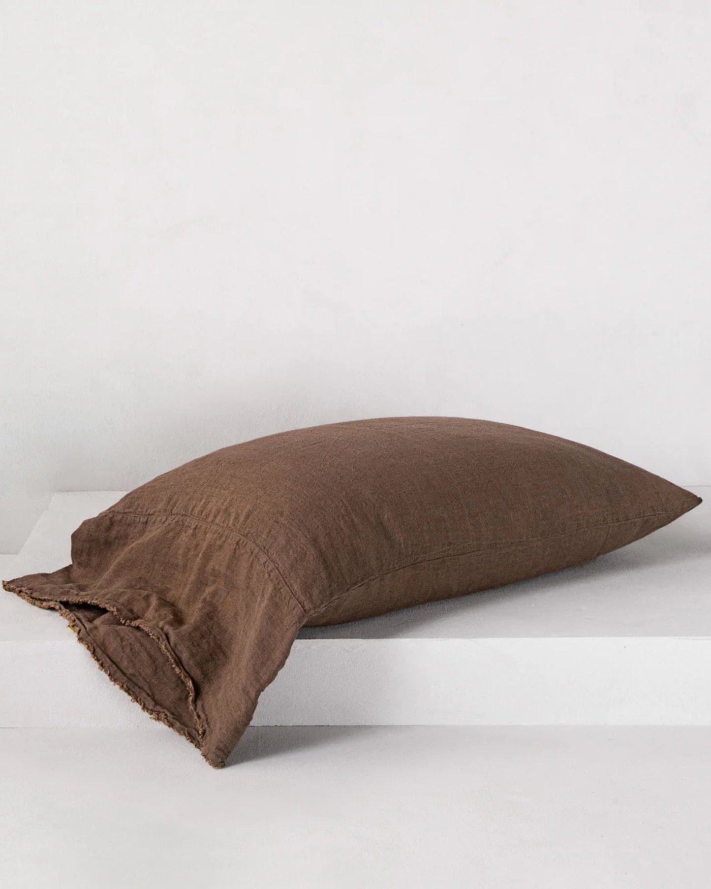 The HALE FLOCCA FLOPPY END PILLOWCASE by Hale Mercantile Co, featuring Flocca hand-tufted edges, rests on a white surface. Its simple, natural texture complements the plain light background, capturing the essence of pure linen bedding.