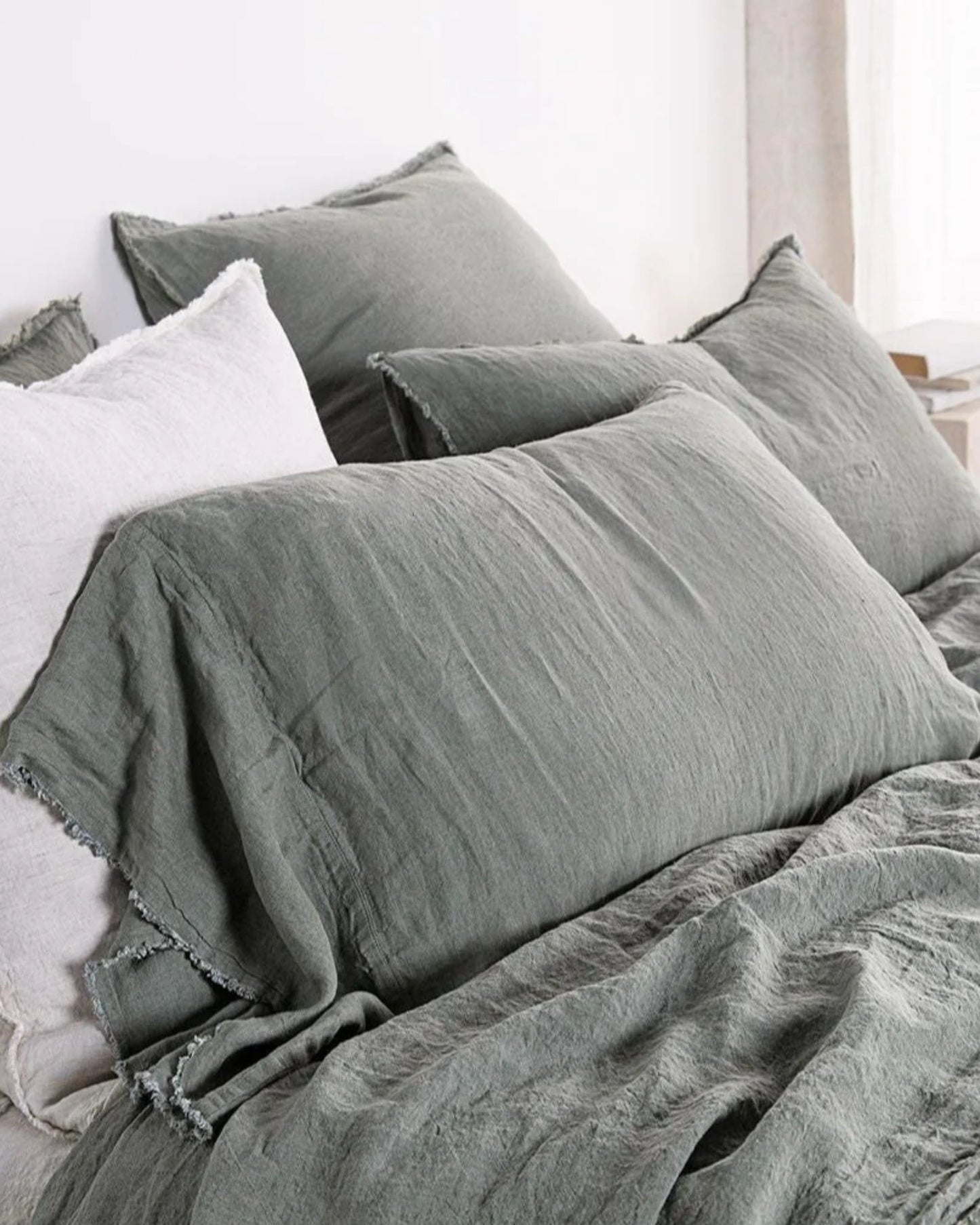 A cozy bed showcases Hale Mercantile Co's HALE FLOCCA FLOPPY END PILLOWCASE in linen, paired with a matching green duvet cover featuring Flocca hand-tufted edges. The pillowcases and duvet boast a soft, textured appearance, creating a calming and inviting atmosphere.