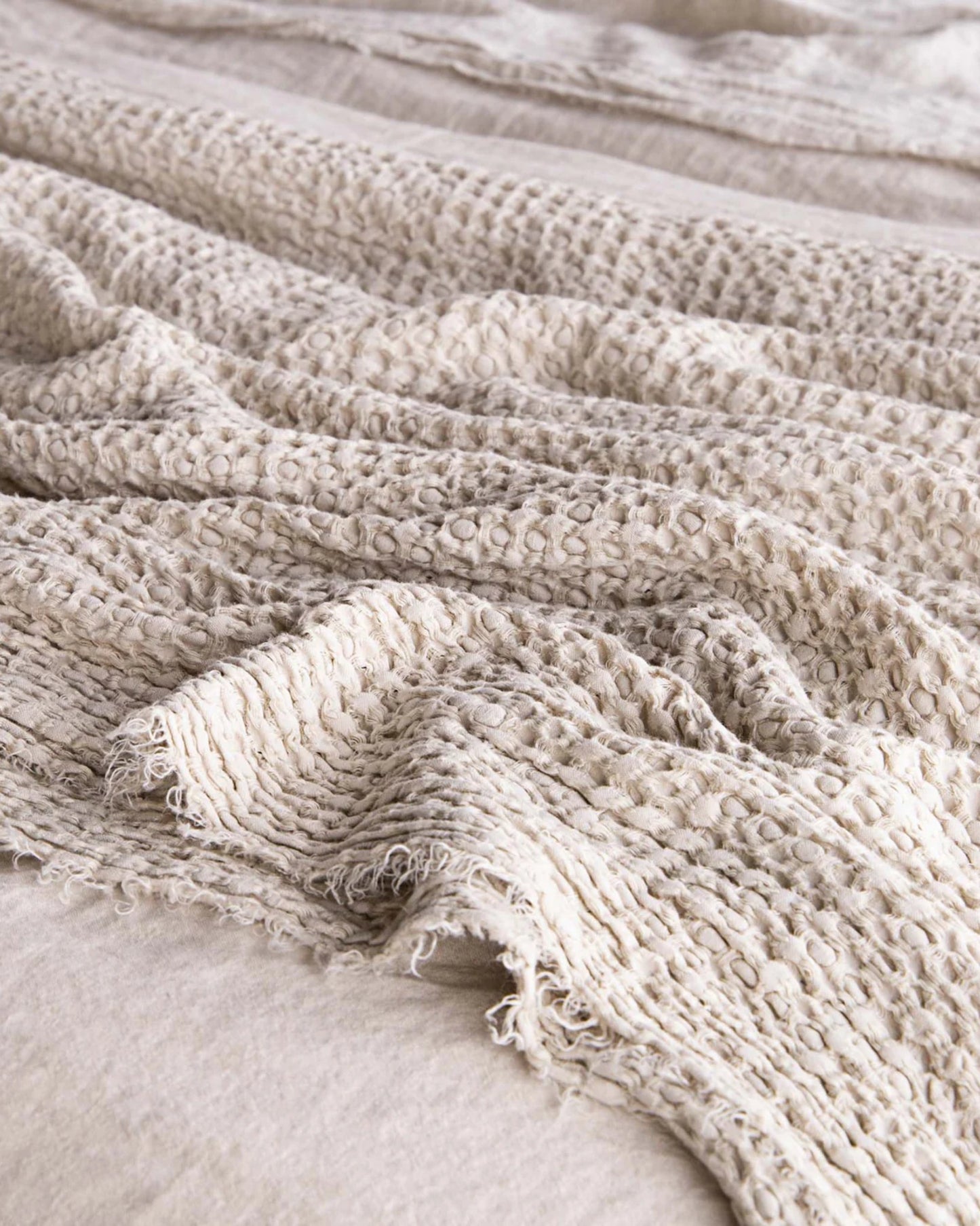 Close-up of the HALE FLOCCA THROW, a cozy and textured linen creation by Hale Mercantile Co. It features a woven pattern with slightly frayed edges. The pure linen blanket is spread out on a surface, creating gentle folds and shadows that embody the essence of luxury throws.