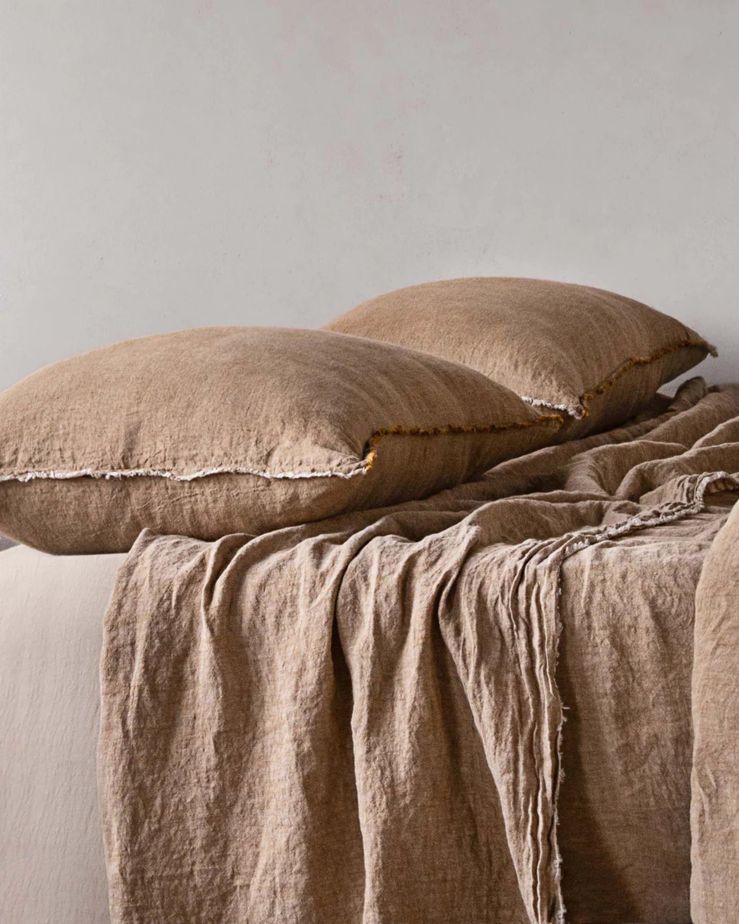 Two fluffy, pure linen pillows rest on a bed with matching beige Hale Mercantile Co HALE STANDARD FLOCCA PILLOWCASES, and a linen blanket draped casually over the edge, creating a cozy and inviting atmosphere.