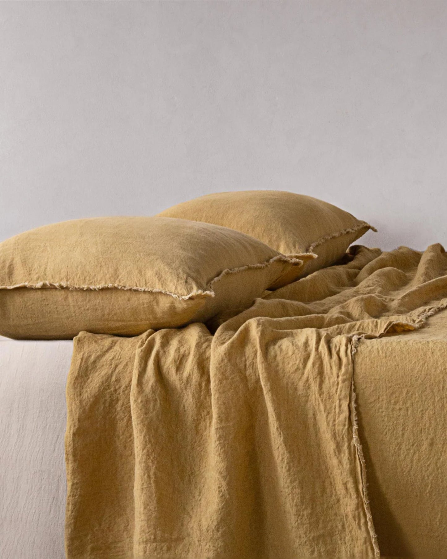 Two pillows featuring the HALE STANDARD FLOCCA PILLOWCASE by Hale Mercantile Co, in a mustard color, rest on a bed complemented by a matching blanket. The handcrafted fabric appears soft and slightly textured, creating a cozy and inviting ambiance against the neutral gray background.