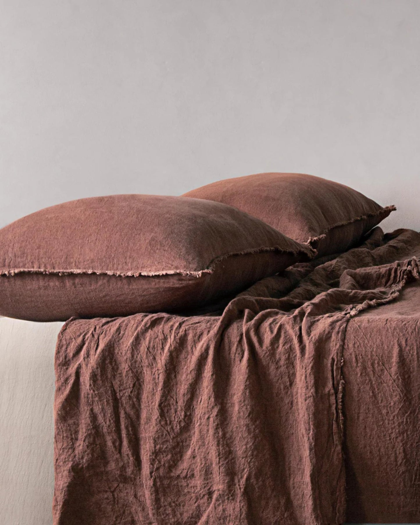 Two large, fluffy pillows with HALE STANDARD FLOCCA PILLOWCASES by Hale Mercantile Co rest on a bed covered with a matching textured brown blanket. The fabric appears soft and inviting against a plain gray wall, creating a cozy and minimalist bedroom setting.