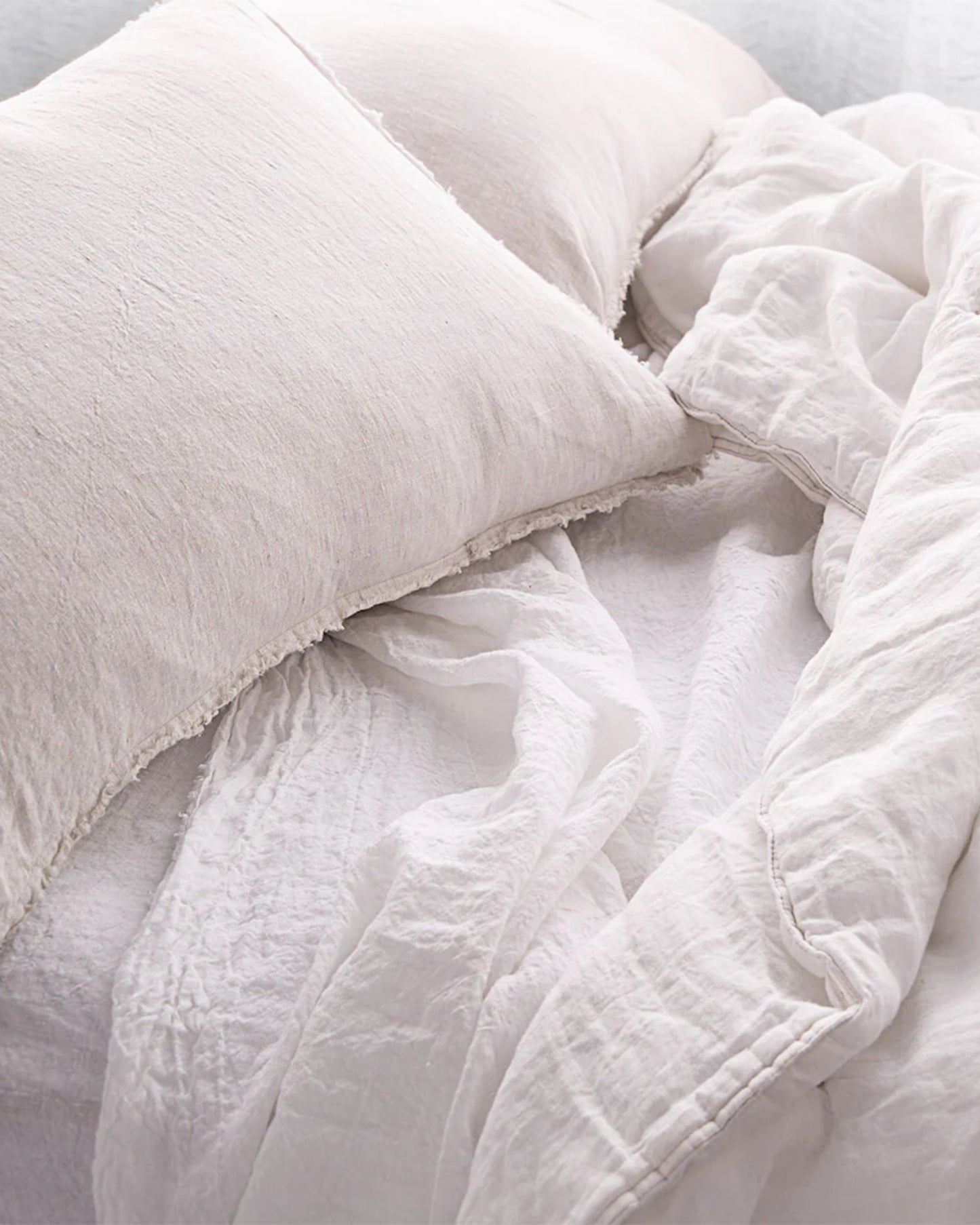 A close-up of a bed featuring HALE STANDARD FLOCCA PILLOWCASE by Hale Mercantile Co, alongside a beige pillow and a crumpled white duvet. The fabric appears soft and cozy, creating an inviting atmosphere.