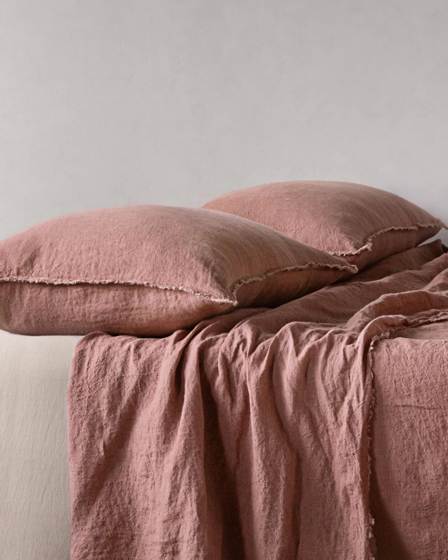 Two HALE STANDARD FLOCCA PILLOWCASES by Hale Mercantile Co, featuring a slightly wrinkled texture for a cozy and inviting appearance, and a soft pink blanket made of pure linen fabric are neatly arranged on a bed against a plain white background.