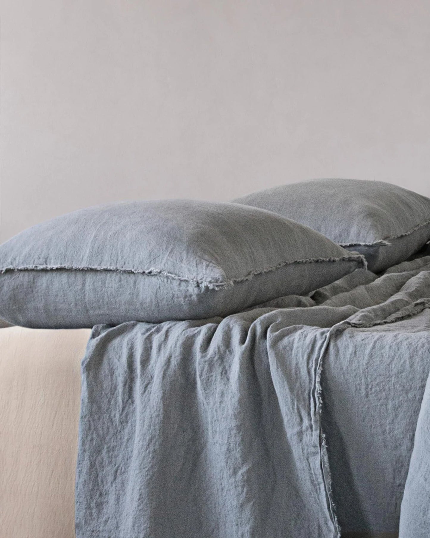 A bed featuring Hale Mercantile Co's HALE STANDARD FLOCCA PILLOWCASE in gray, paired with a matching blanket, creates a minimal and cozy atmosphere. The smooth texture of the pure linen adds an elegant and relaxed feel to the setup, enhancing its understated charm.