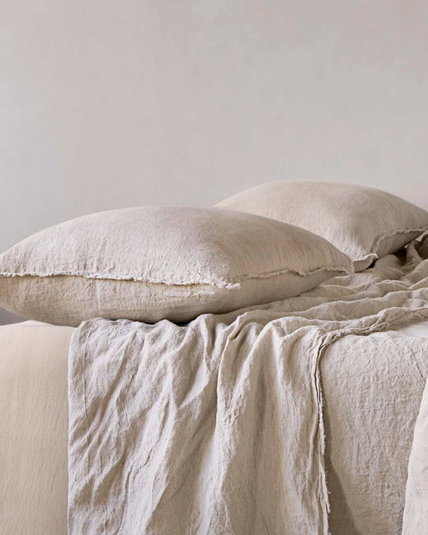 The bed features two large pillows with handcrafted HALE STANDARD FLOCCA PILLOWCASES by Hale Mercantile Co, elegantly textured in beige. These pillows rest on the bed, harmonizing with draped sheets in matching tones to establish a serene and cozy ambiance.