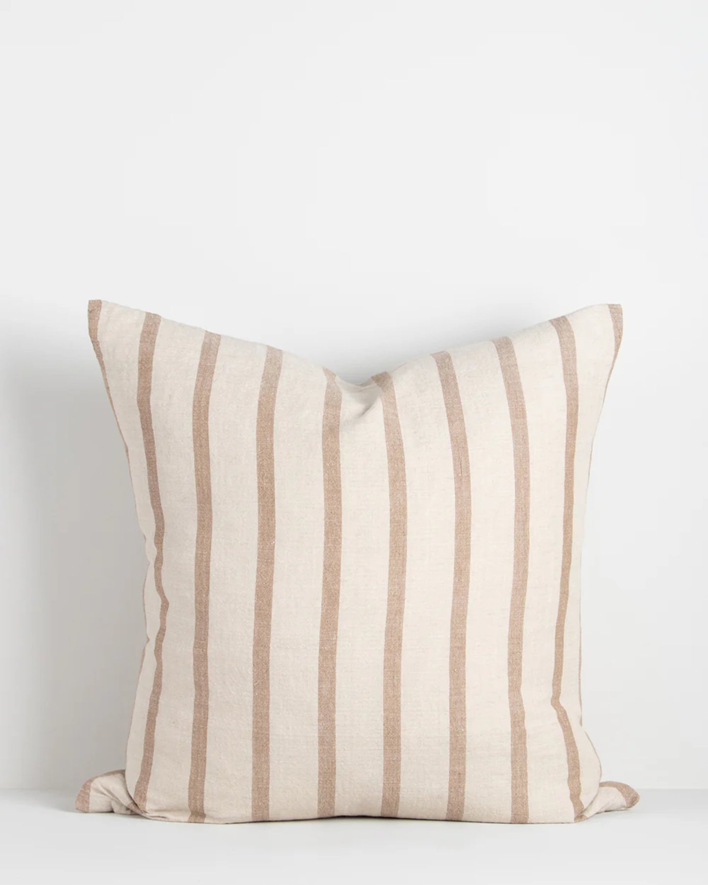 A Baya Hampton Cushion, featuring beige and white vertical stripes, stands upright against a plain white background. Made from natural fibers, it embodies a simple and minimalist design with a casual stripe aesthetic.