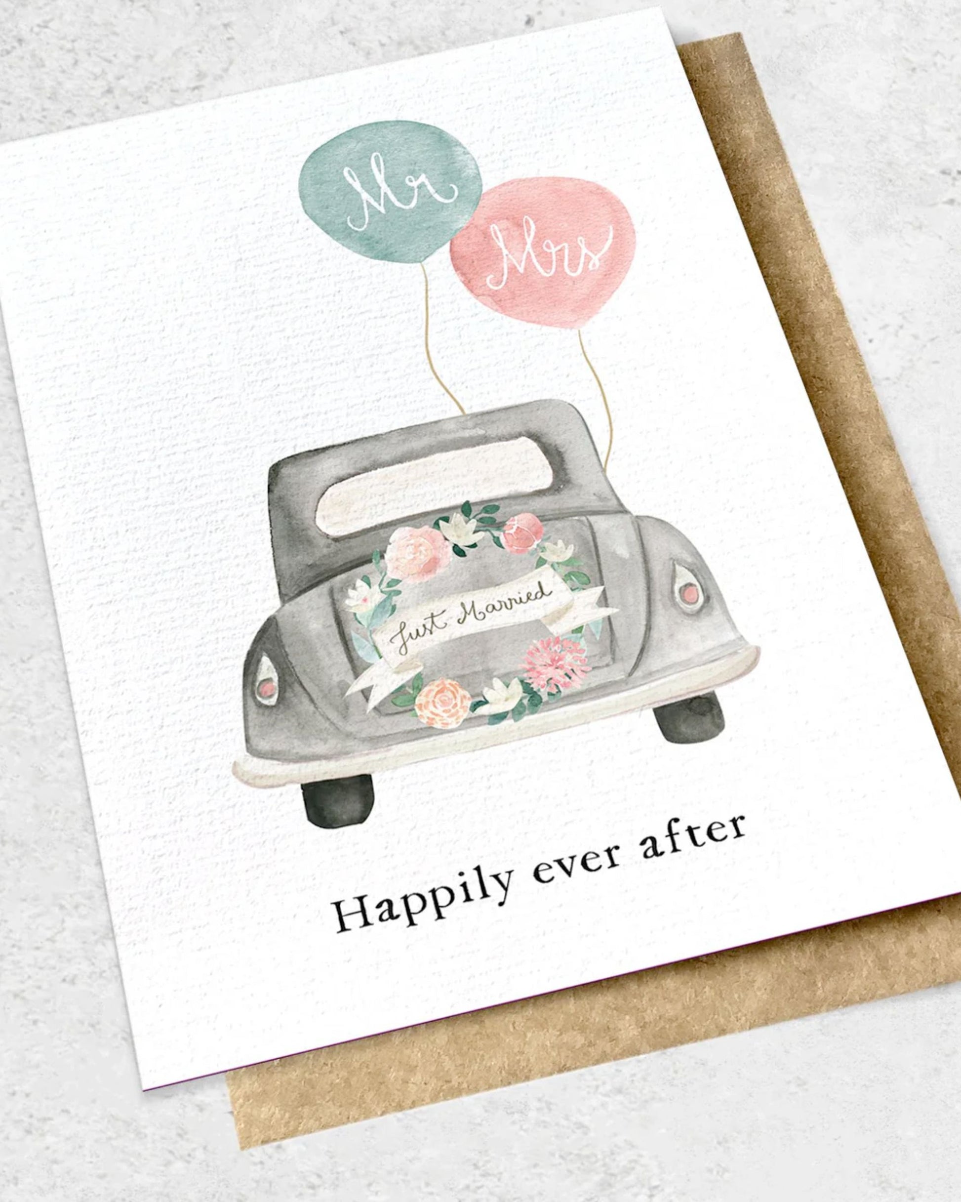 Introducing the "HAPPILY EVER AFTER - GREETING CARD" by Ink Bomb: This exquisite wedding card showcases an illustration of a car decorated with flowers and a "Just Married" sign. Attached to the car are two balloons labeled "Mr" and "Mrs." Below, you'll find the message "Happily Ever After." The card comes with a premium textured kraft envelope, adding an elegant touch.