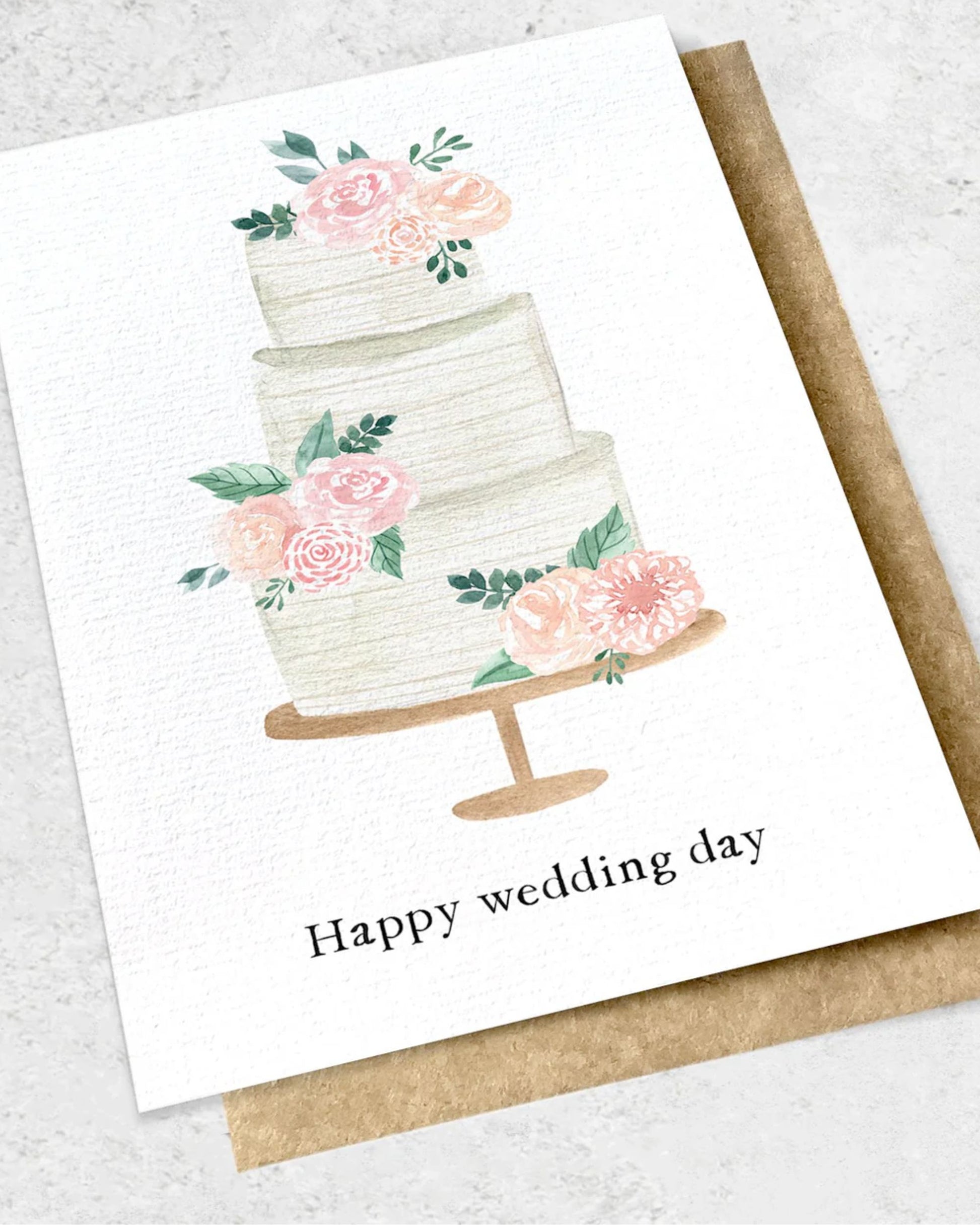 An illustration of a three-tiered wedding cake decorated with pink and peach flowers along with green leaves is elegantly displayed on a golden stand. Beneath it, the words "Happy Wedding Day" embellish a premium textured card from Ink Bomb's HAPPY WEDDING DAY - GREETING CARD collection, accompanied by a classic kraft envelope in the background.