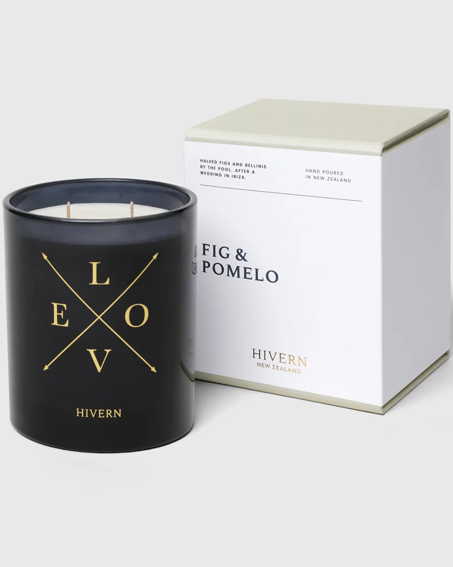 A black candle labeled "LOVE" with crossed arrows and the brand name "Hivern" is accompanied by a white box that features the description "FIG & POMELO," emphasizing its New Zealand home fragrance origins. The box highlights notes of waxed figs and bellini wedding, is hand-poured, and boasts a 55-hour burn-time for optimal candle care.