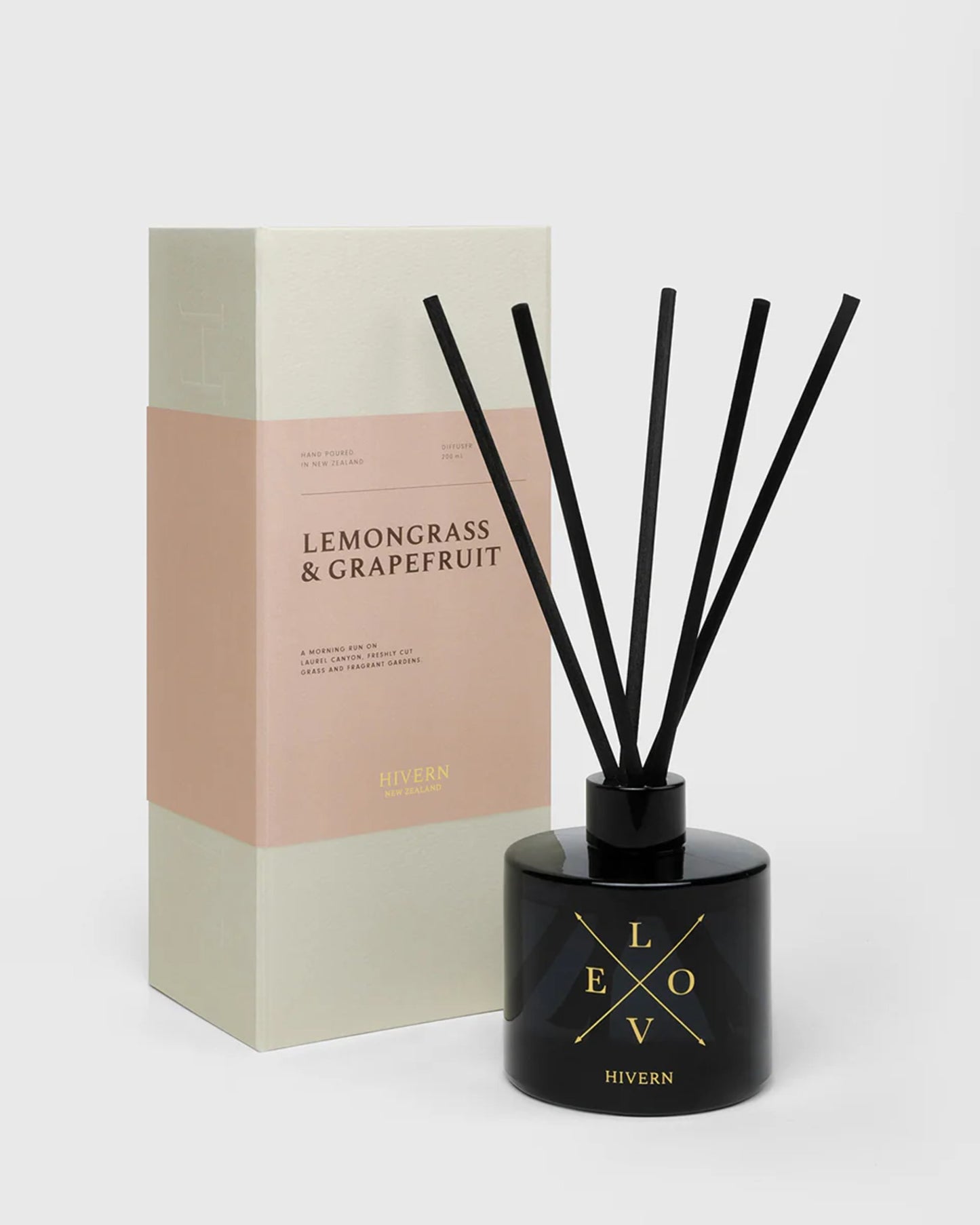 A black diffuser bottle from Hivern, labeled LOVE, stands with five silk fibre reeds for enhanced scent dispersion. It's displayed in front of a beige and white box featuring sections of pink and white with gold text, labeled LEMONGRASS & GRAPEFRUIT by Hivern Home Fragrance.