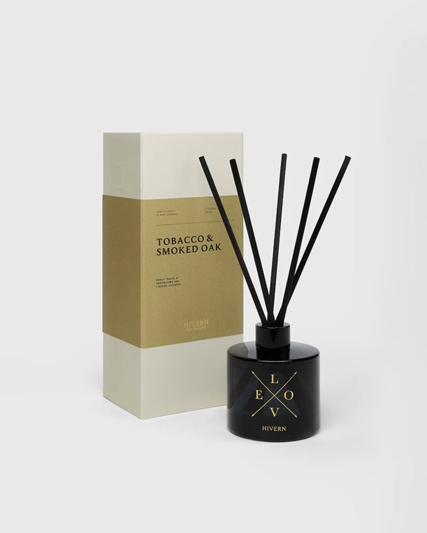 A black diffuser bottle with silk fiber reeds, branded as the Hivern Diffuser by Hivern, stands next to a beige and white box displaying "Tobacco & Smoked Oak" text. Designed for optimal scent dispersion, it elegantly complements the plain light gray background.