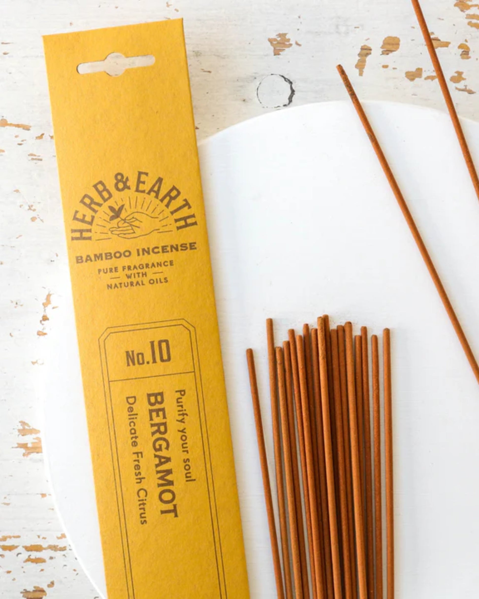 A pack of Herb and Earth's Incense - Herb and Earth in the No. 10 Bergamot variety provides a pure fragrance with a delicate fresh citrus scent and minimal smoke. The image displays brown incense sticks next to the yellow packaging on a slightly distressed white surface.