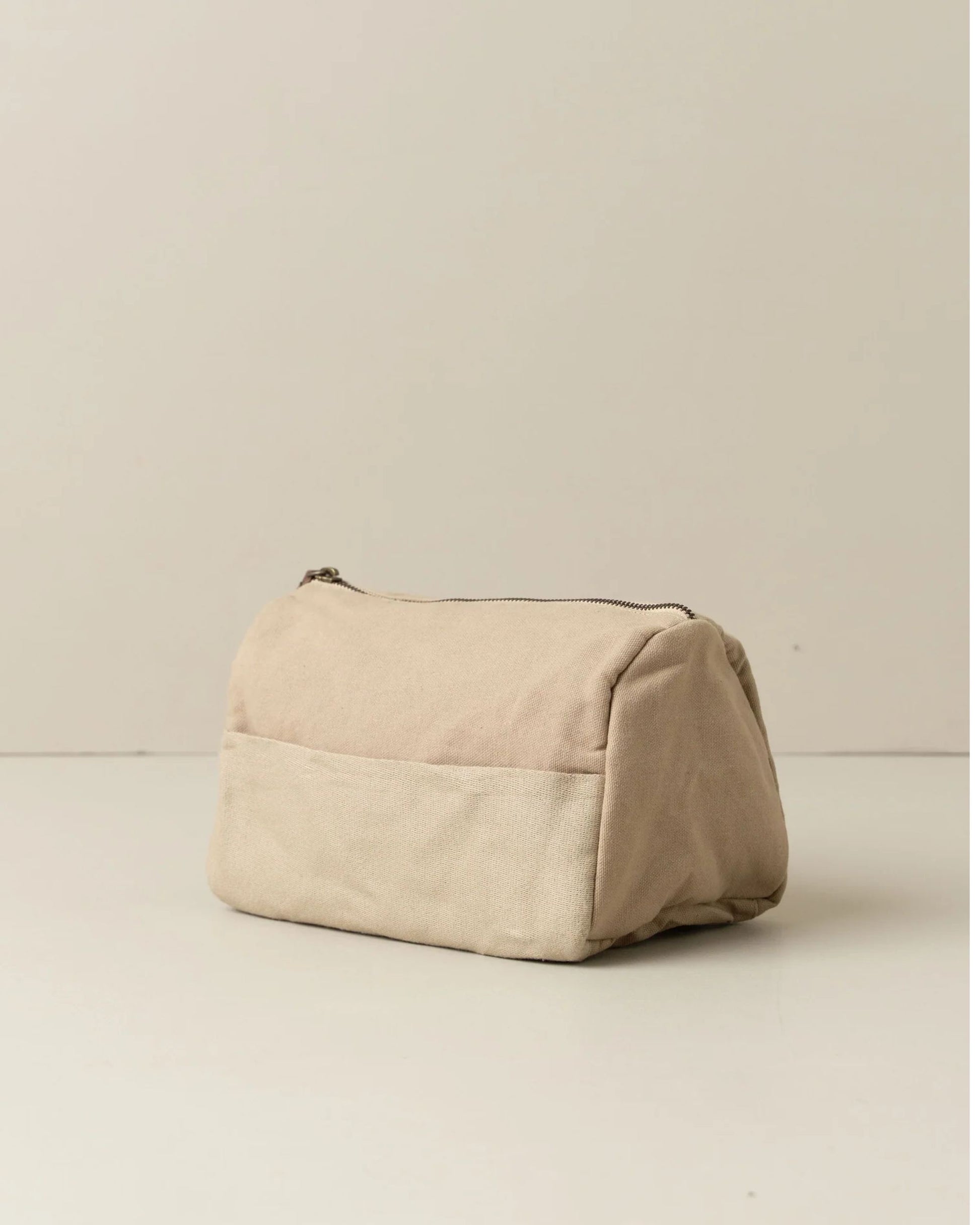 The JOURNEY TOILETRY CANVAS BAG by Saarde, made with beige fabric and genuine leather detailing, provides a chic solution for your toiletry essentials. Its rectangular shape with soft edges and a convenient zipper top incorporates a useful front pocket for enhanced organization on any adventure.