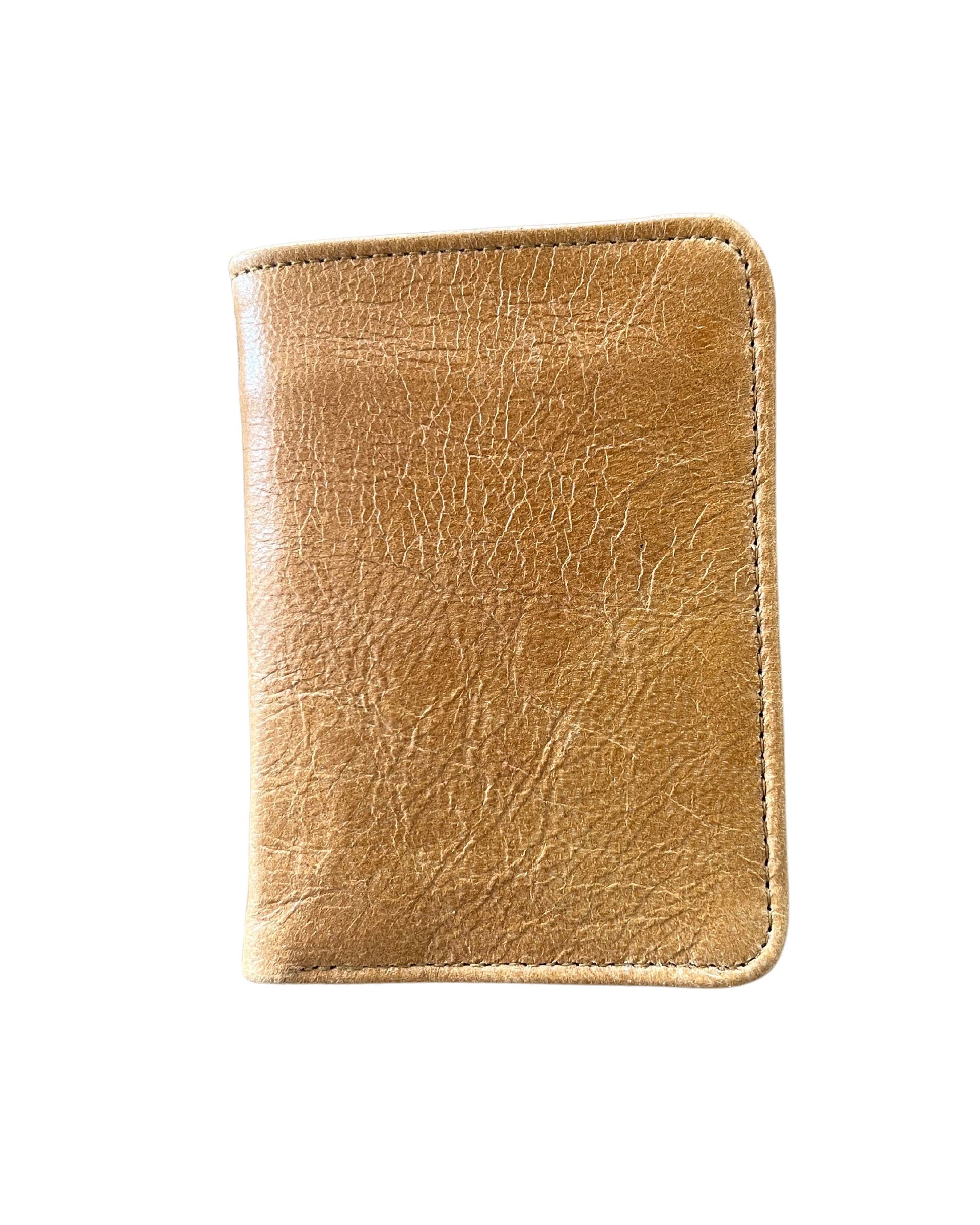 A genuine LEATHER WALLET by The Workroom, with its character-rich creases in weathered brown, lies closed against a stark white background, evoking the stories nestled within its card slots.