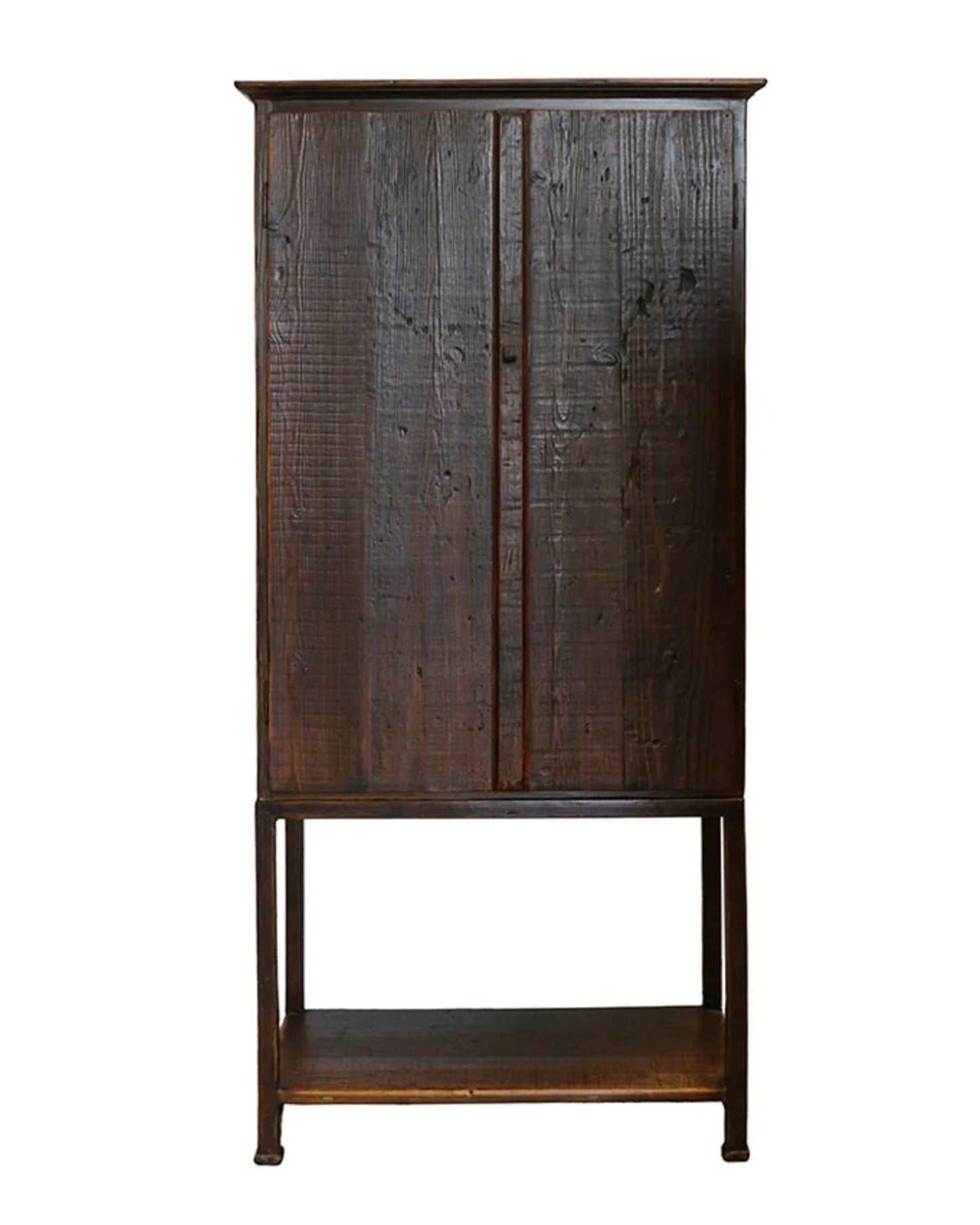 The LITCHFIELD TALL OAK CABINET by CC interiors is a tall, solid oak piece with two doors and a minimalist design, standing elegantly on four slender legs to exude rustic charm. Its rich, textured finish is beautifully complemented by an open shelf at the bottom.