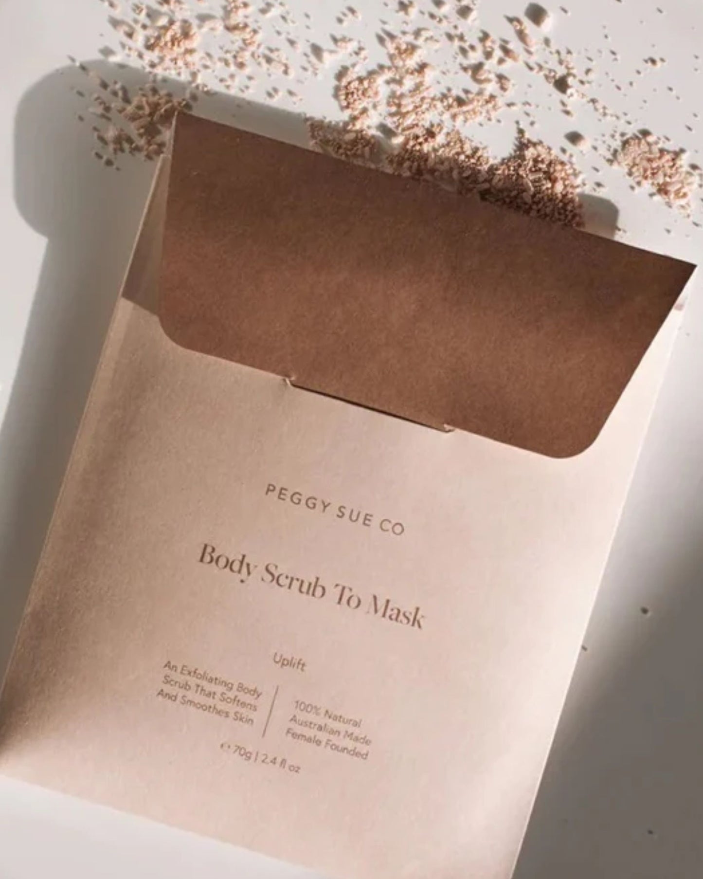 An open packet labeled PEGGY SUE - BODY MASK rests on a surface, its contents delicately spilled out. The packaging features a soft, neutral color, inviting you to savor a tranquil self-care experience with Peggy Sue.