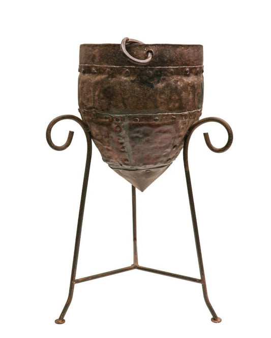 The ORIGINAL CHAMPAGNE BUCKET by Hawthorne boasts a rustic, handcrafted design made from recycled iron, perched on a decorative wrought iron stand with curled legs, imparting the medieval charm of an industrial piece.