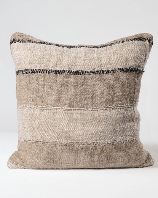 The RETREAT CUSHION from the Eadie brand displays a cotton/linen blend in natural and ivory tones, with black accents. Its textured, woven fabric features horizontal stripes against a plain white background, highlighting its natural, earthy appearance.