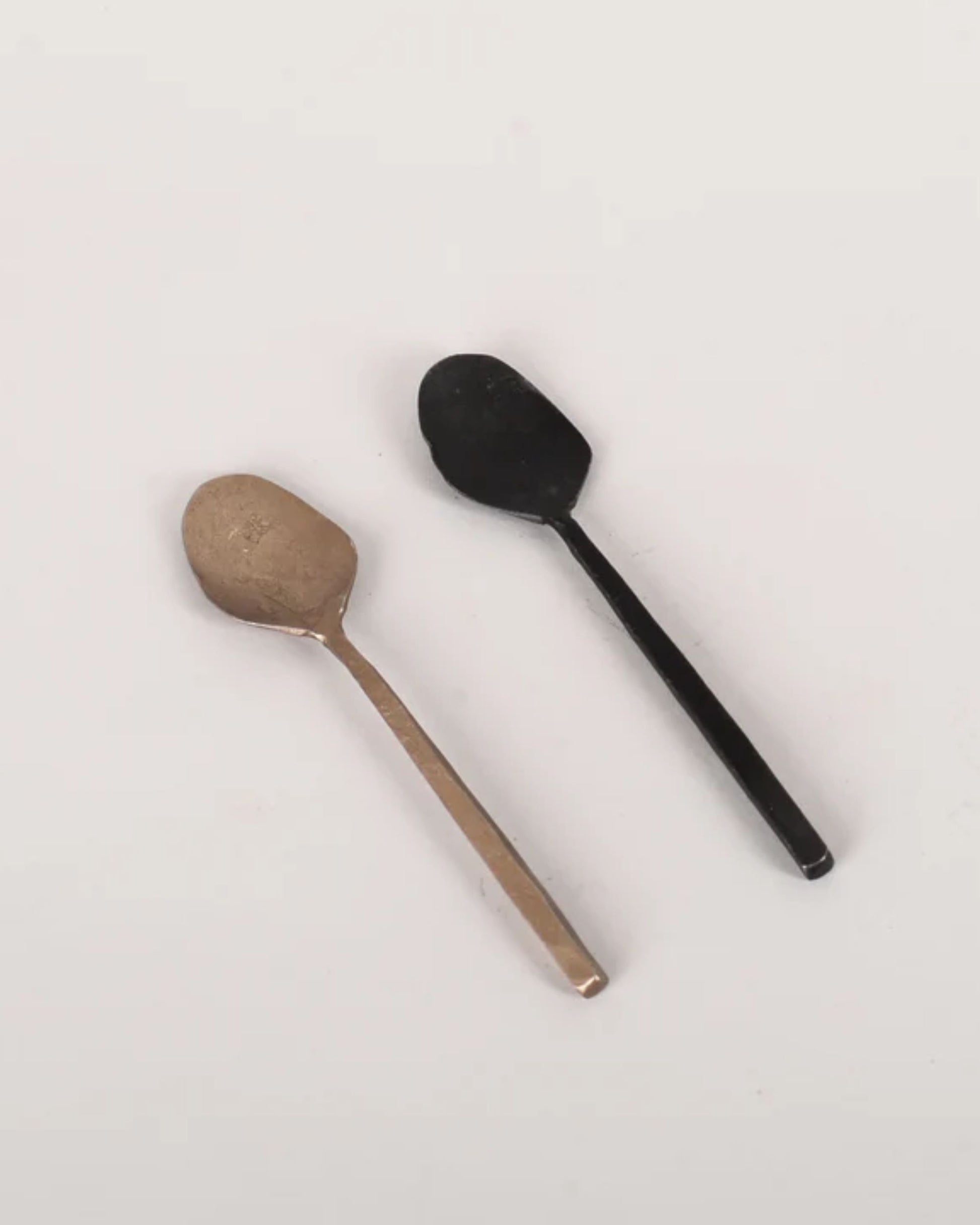 Two ANTIQUE SALT SPOONS from New Direction rest on a light background. One is silver, the other black, both featuring a simple, minimalist design. Their vintage charm adds a touch of elegance, making them perfect as a decorative accent in any setting.