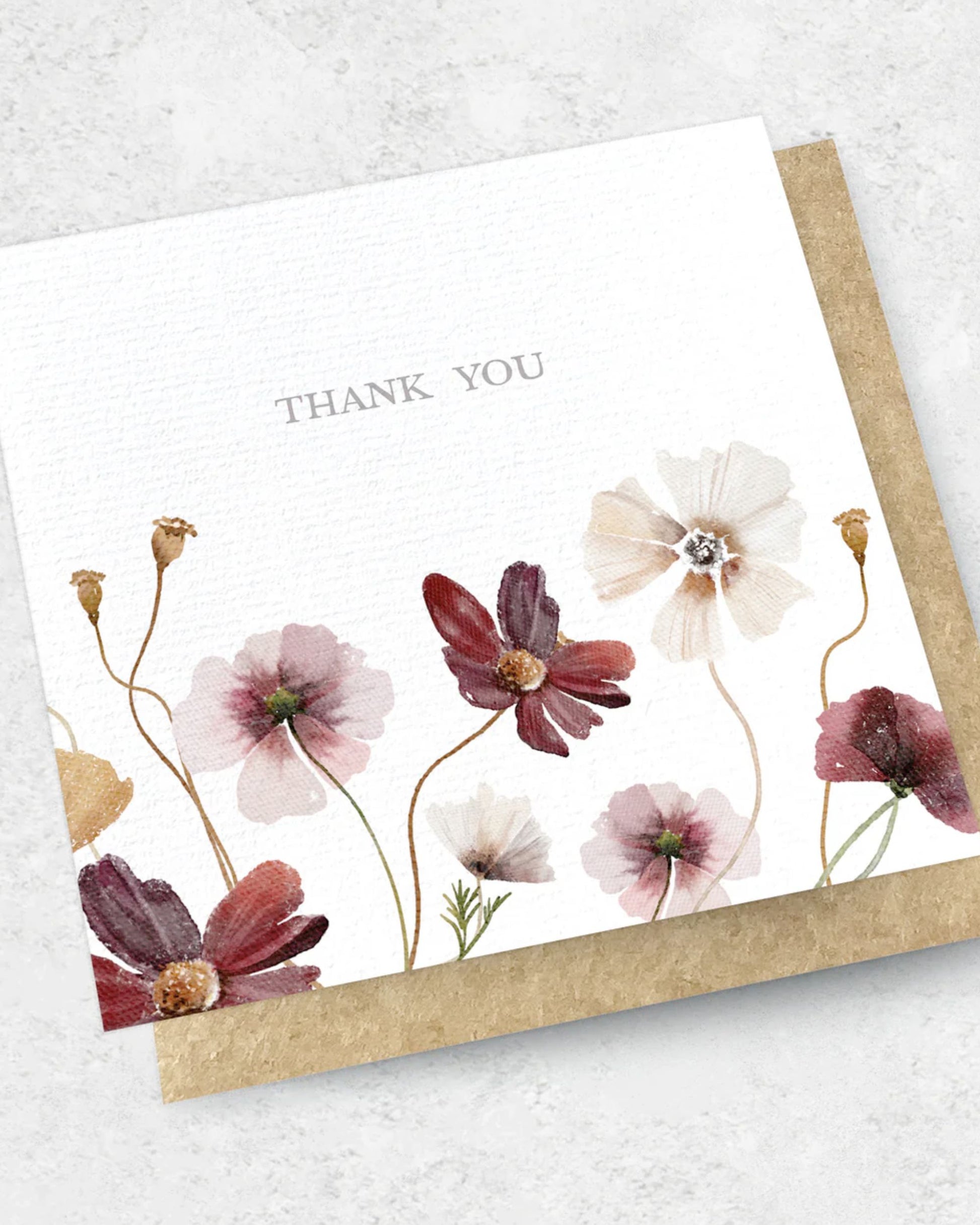 Introducing the THANK YOU FLOWERS - GREETING CARD by Ink Bomb. This exquisite card features watercolor flowers in vibrant shades of red, pink, and white, elegantly set against a pristine white background. The words "THANK YOU" are gracefully centered at the top, perfectly complemented by an elegant kraft envelope.