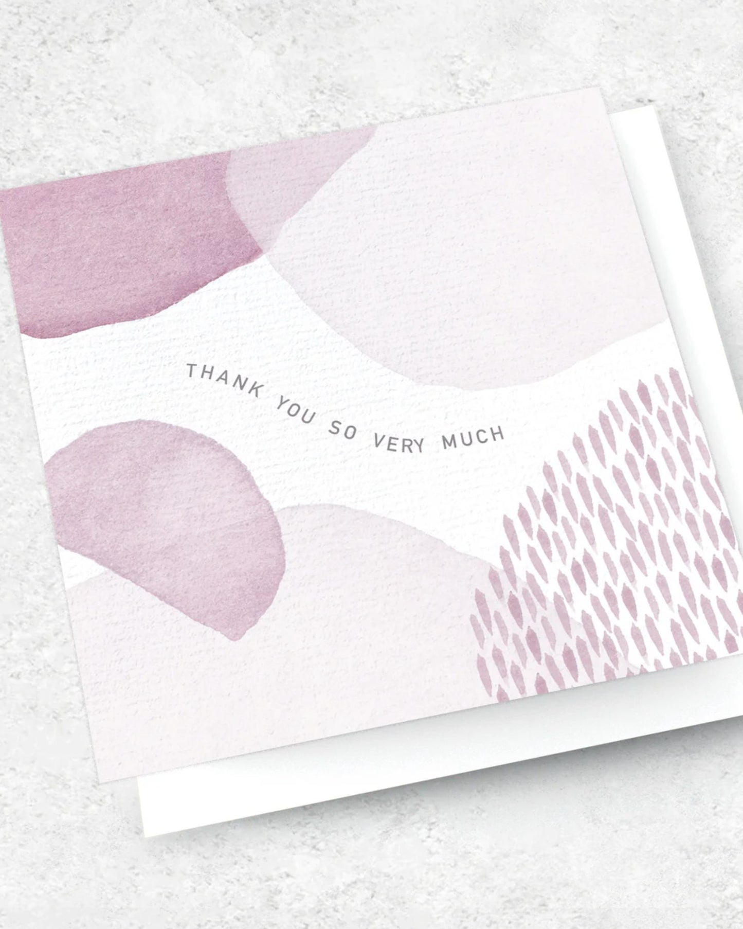 The Ink Bomb premium textured THANK YOU SO VERY MUCH greeting card showcases abstract pink and gray watercolor designs. The central text states, "THANK YOU SO VERY MUCH." Accompanied by a white envelope, the card is set against a textured light gray background.