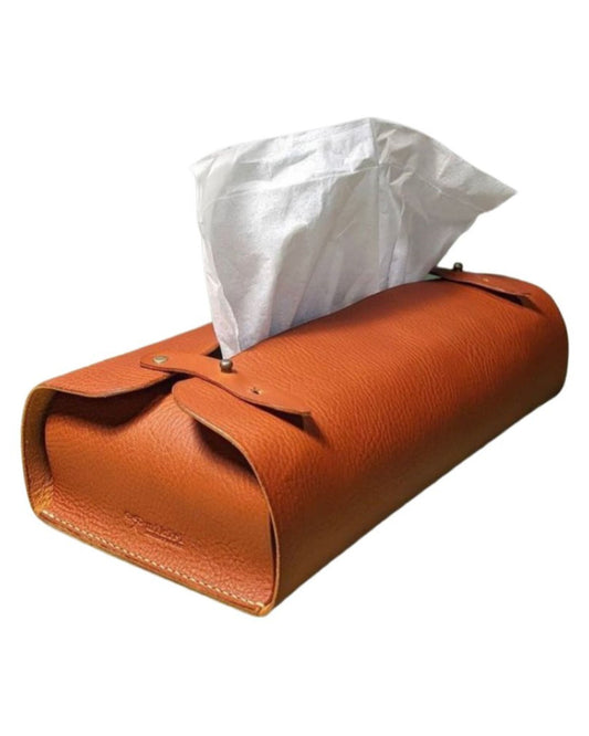 Introducing the Leather Tissue Box Holder by The Workroom, a luxurious room accessory crafted from premium brown leather. Its sleek rectangular design features one white tissue peeking through the top opening, beautifully accented by small silver studs and detailed stitching along the edges. This elegant piece is sure to effortlessly elevate any space.