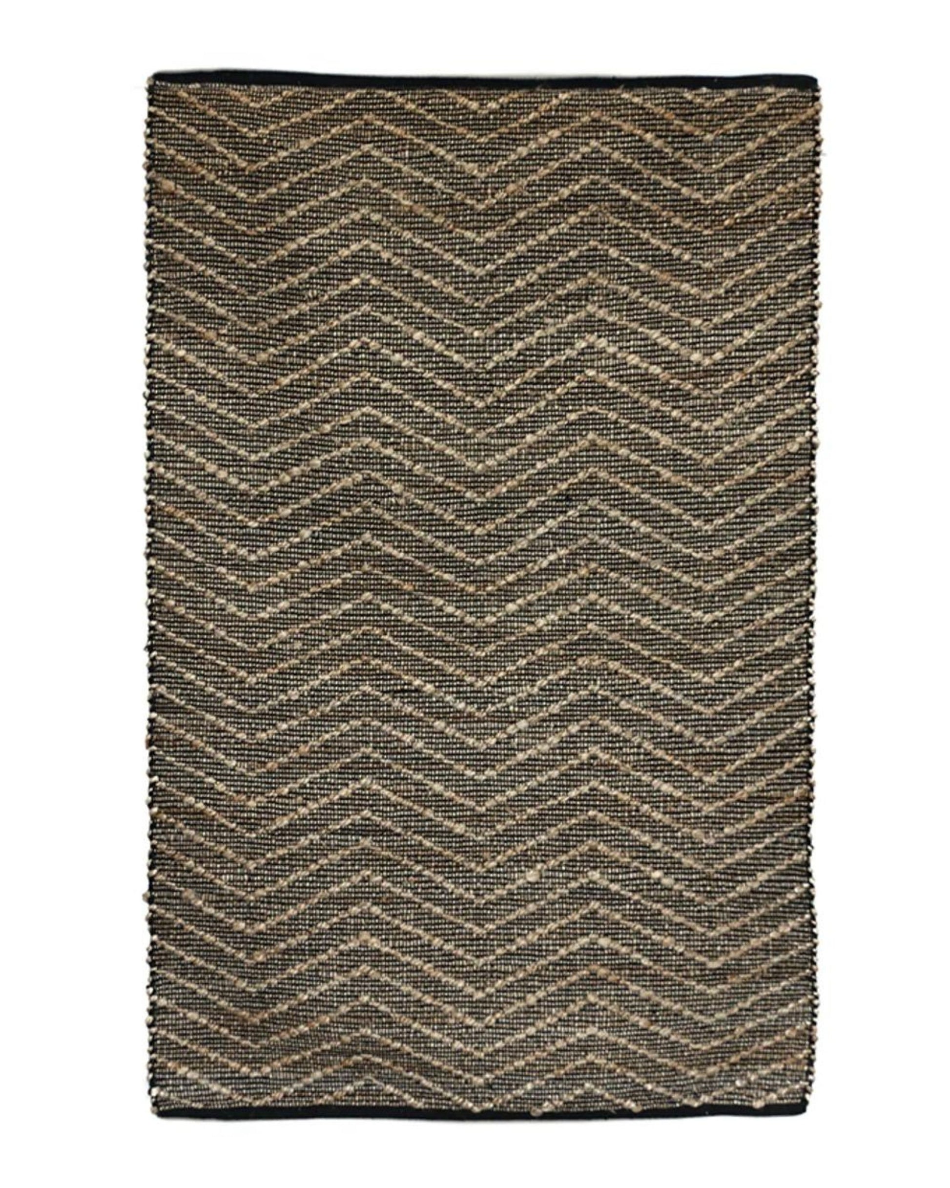 The ZIGGY JUTE/COTTON RUG by CC interiors is a rectangular piece featuring a chevron pattern in brown and black tones. This eco-friendly rug boasts neatly finished edges and showcases a coarse, natural texture.