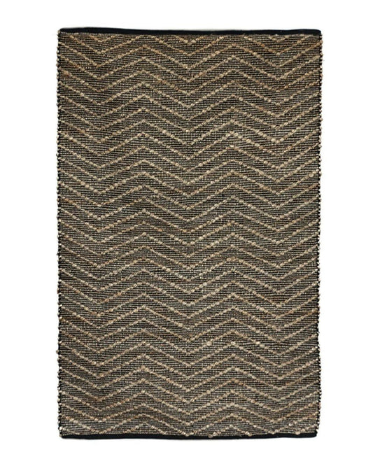 The ZIGGY JUTE/COTTON RUG by CC interiors is a rectangular piece featuring a chevron pattern in brown and black tones. This eco-friendly rug boasts neatly finished edges and showcases a coarse, natural texture.